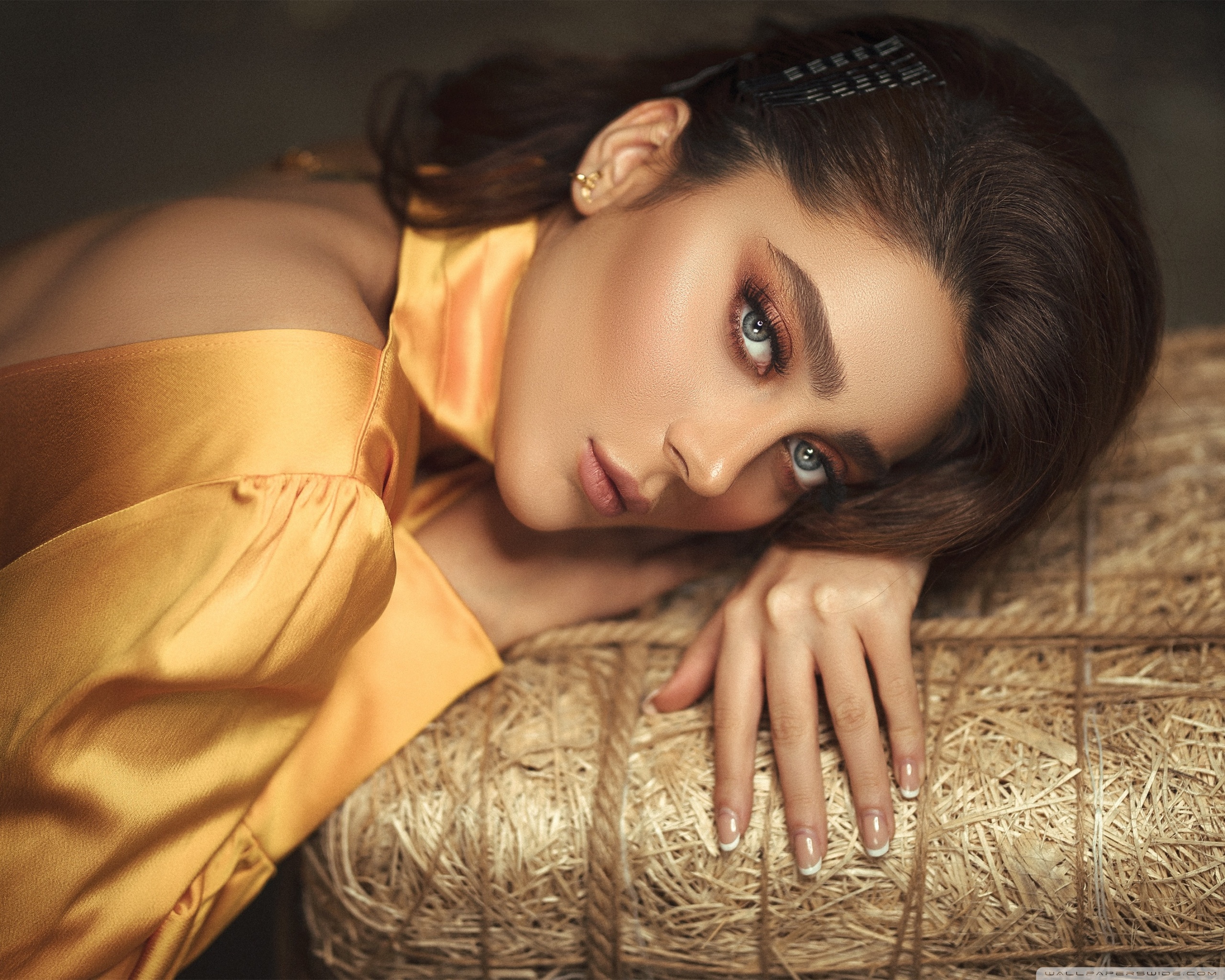 A beautiful woman with a bright make-up and long hair is lying on a bale of hay. - Makeup