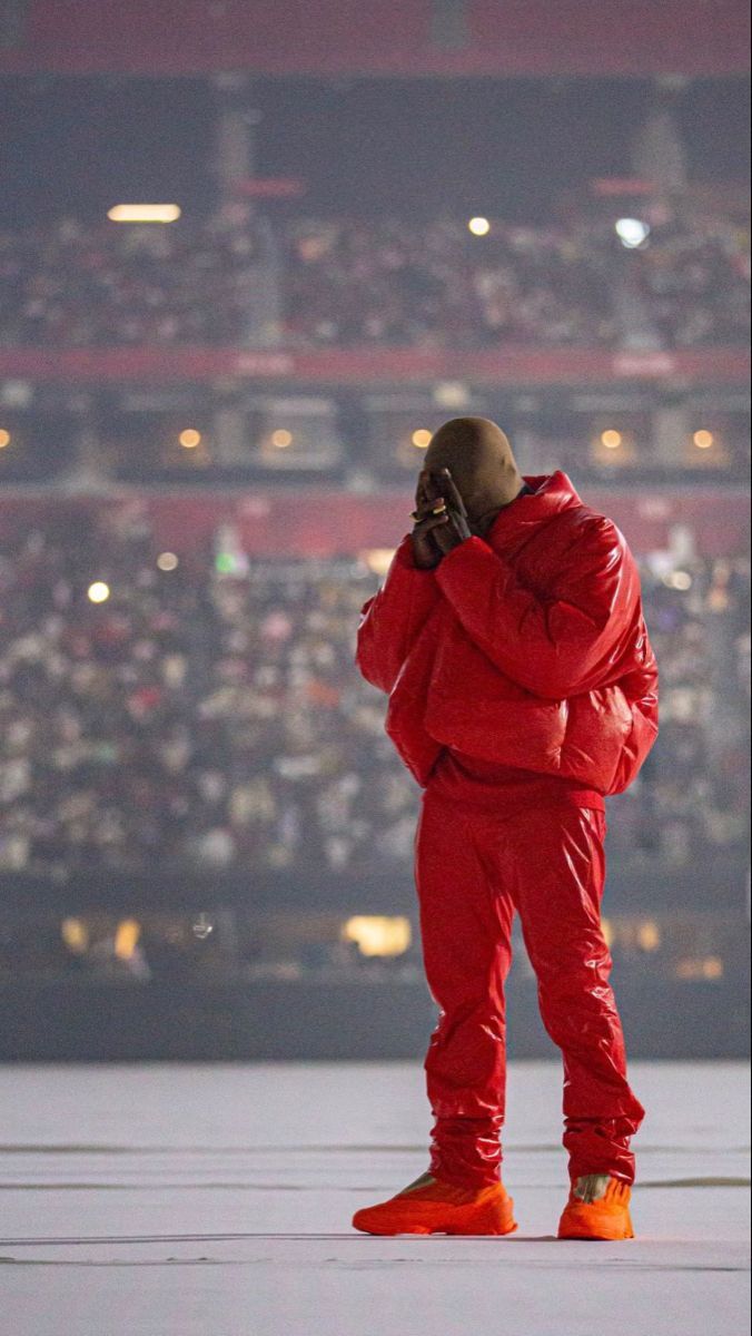 Kanye West in a red outfit standing in front of a crowd - Kanye West