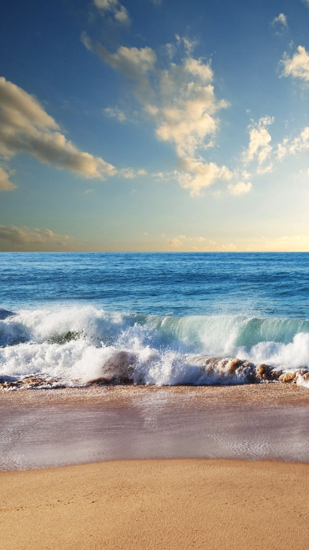 A wave crashes on the beach under a blue sky. - Beach, coast