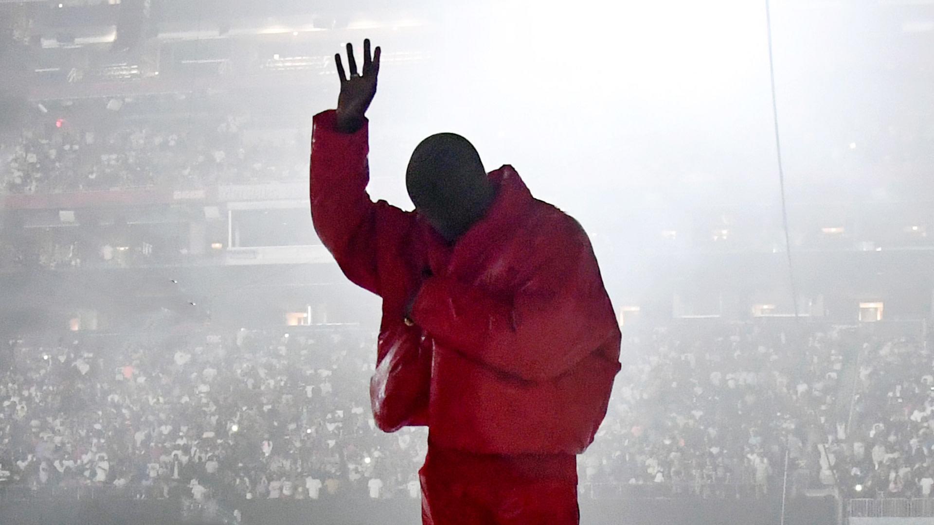 Kanye West in a red suit waves to the crowd - Kanye West