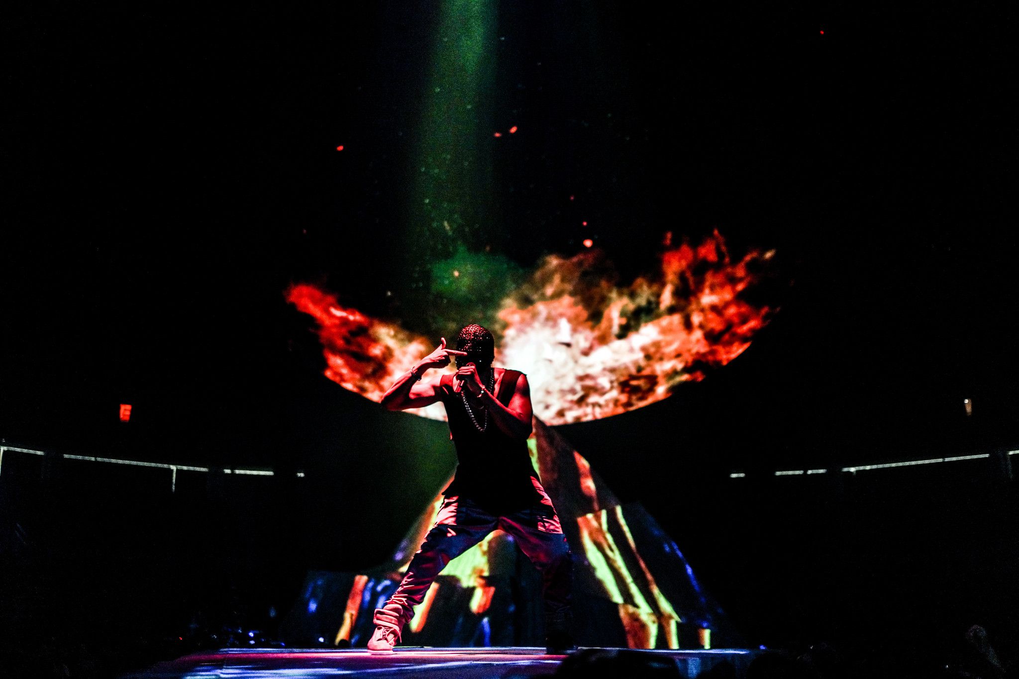 A man standing on stage with fire behind him - Kanye West