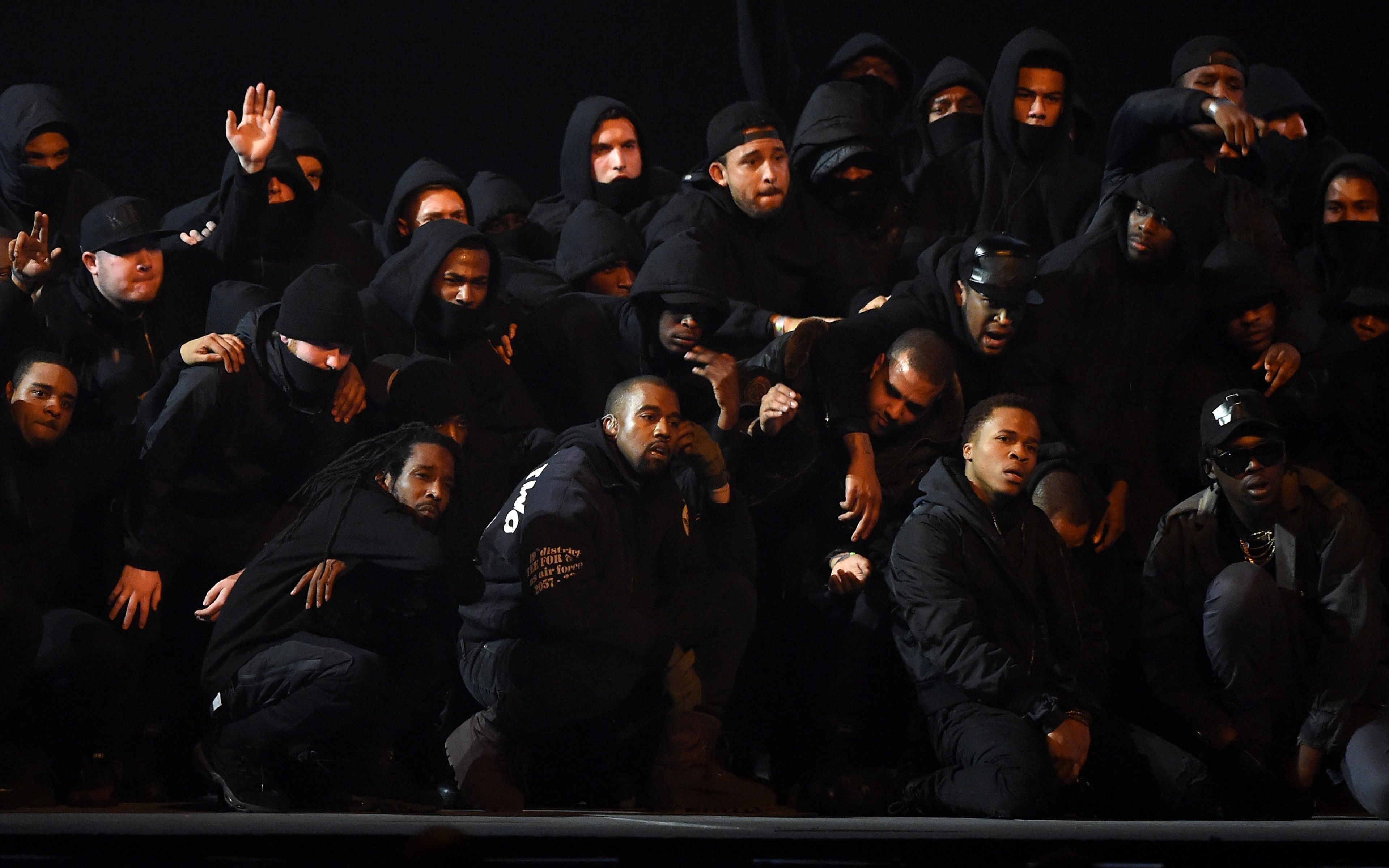 Kanye West performs with a group of people wearing black hooded sweatshirts - Kanye West