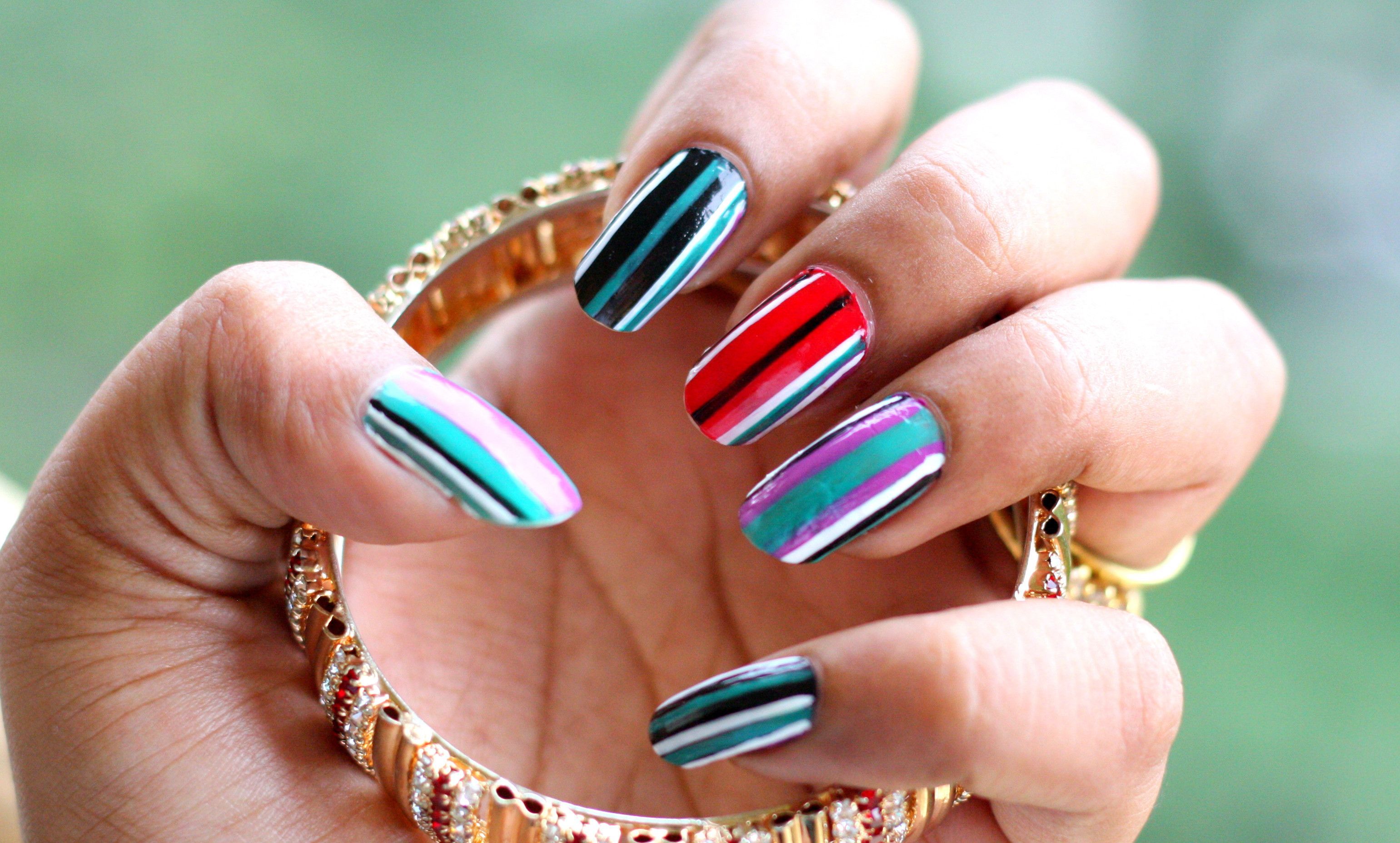 A woman's hand with colorful nail polish holding a gold bracelet. - Nails
