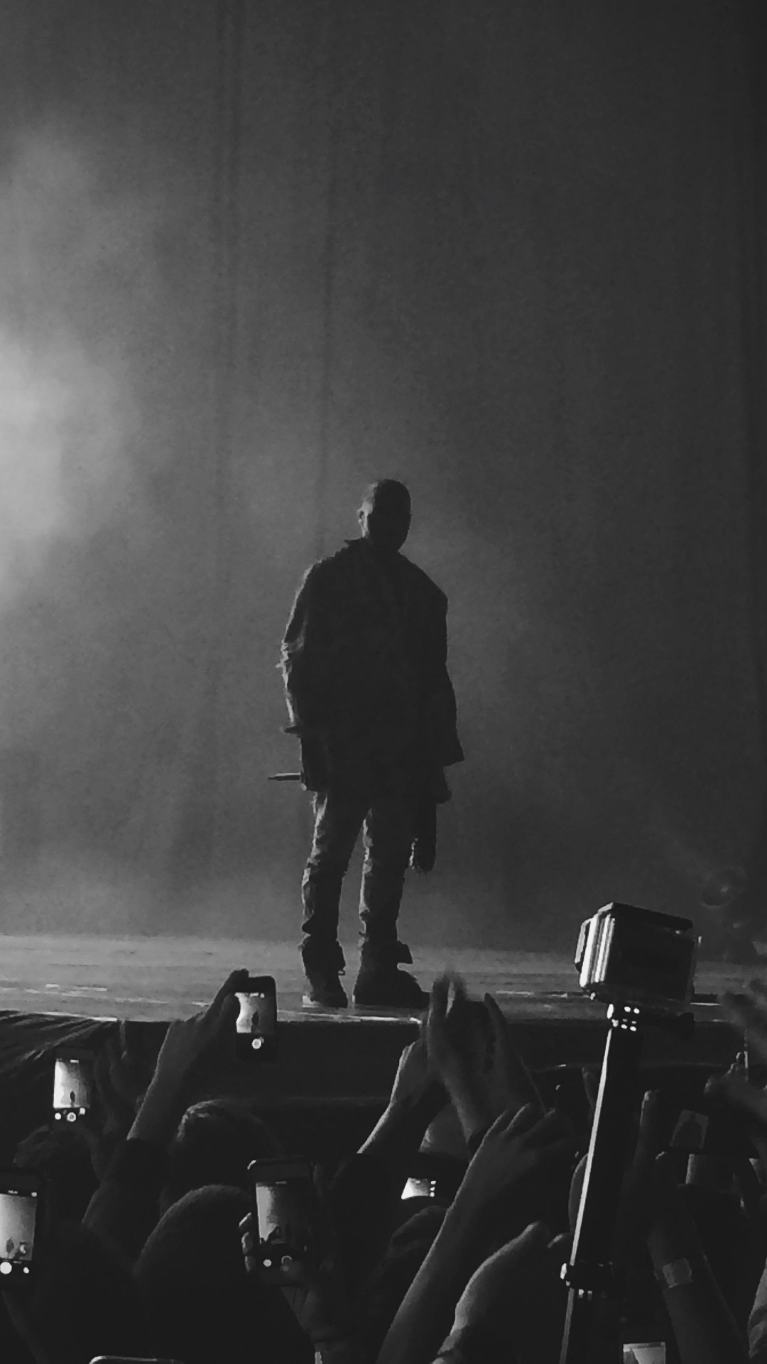 A man standing on stage with people taking pictures - Kanye West