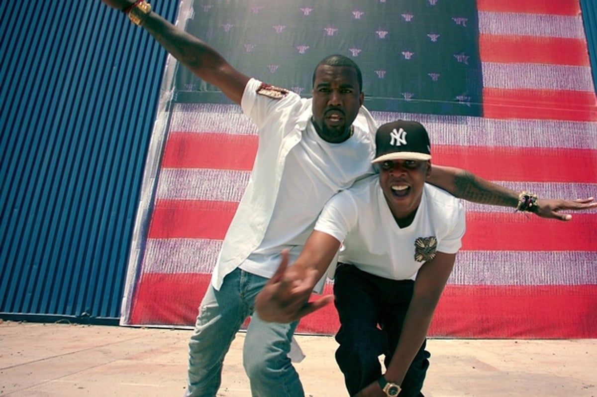 Two men standing next to a large american flag - Kanye West