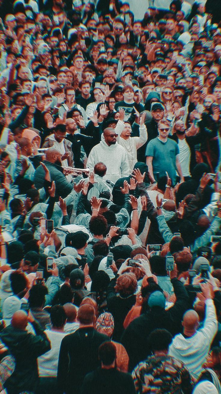 A large crowd of people are surrounding a man in a white shirt. - Kanye West