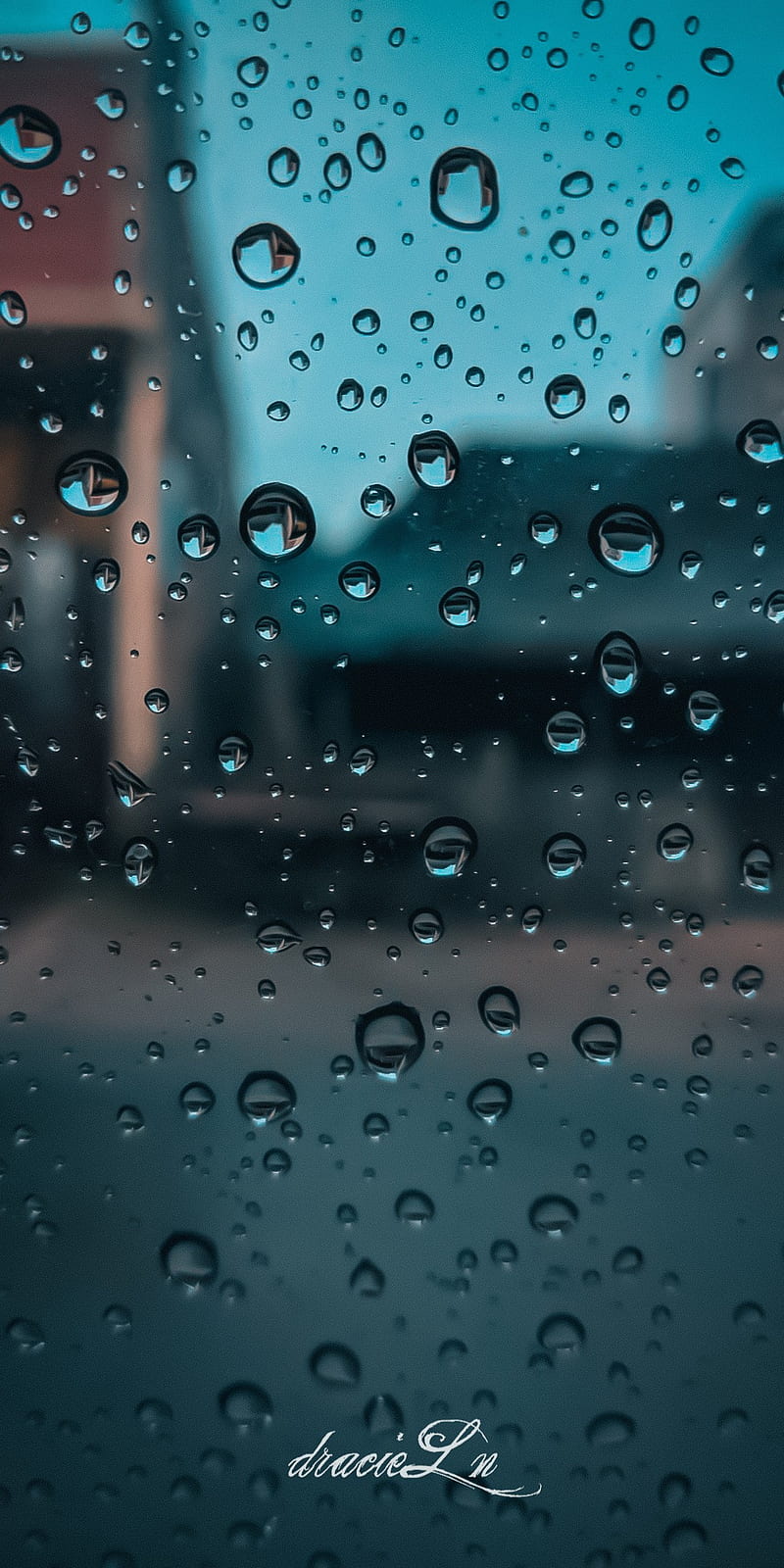 A window with raindrops on it and buildings in the background - Rain