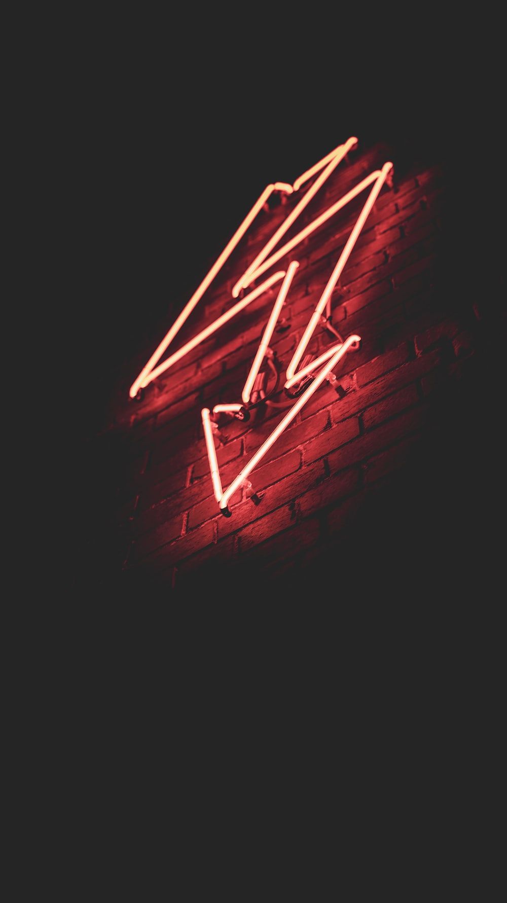 A neon sign of lightning bolt on a brick wall - Neon red