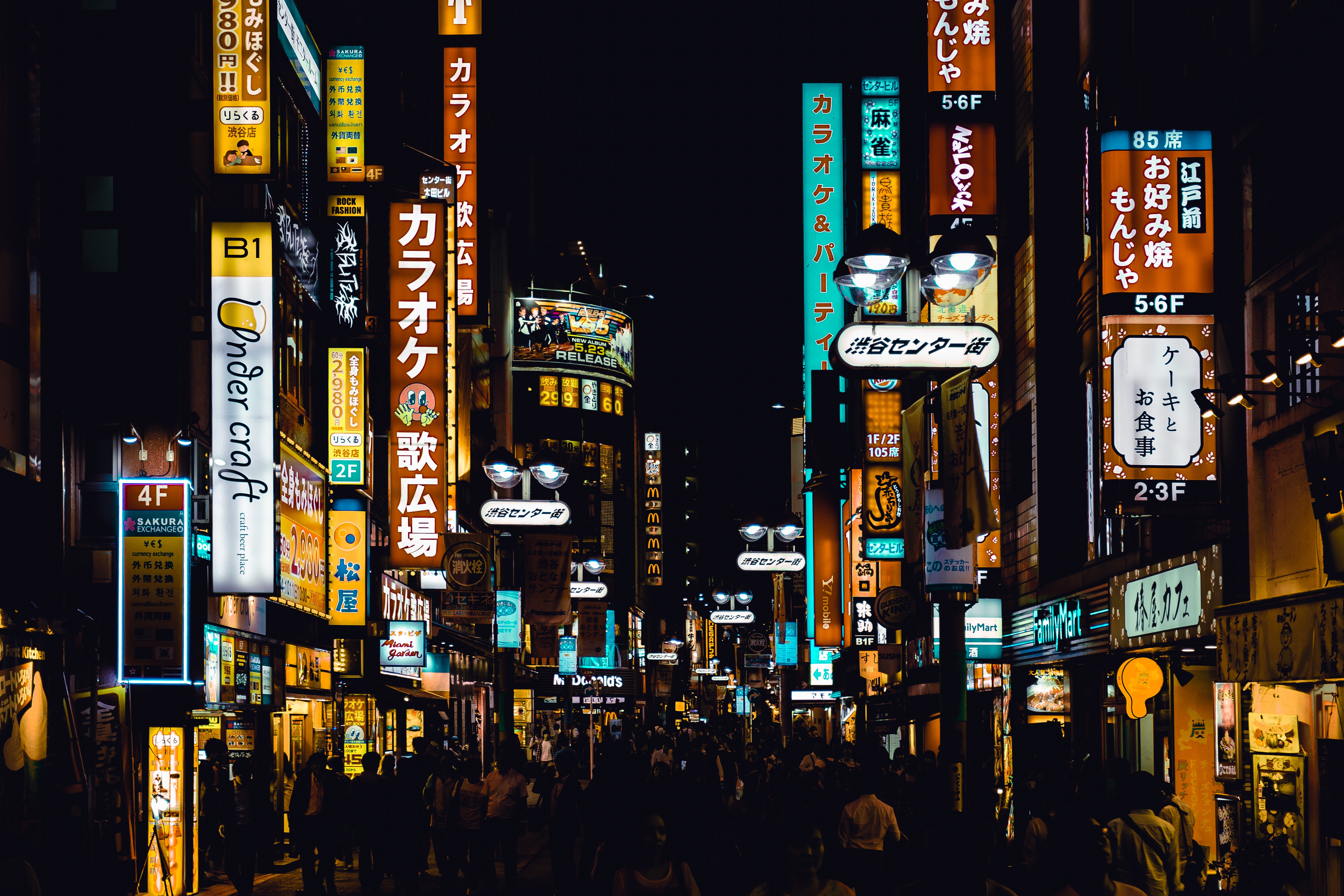 A crowded street at night with bright signs all around. - Tokyo