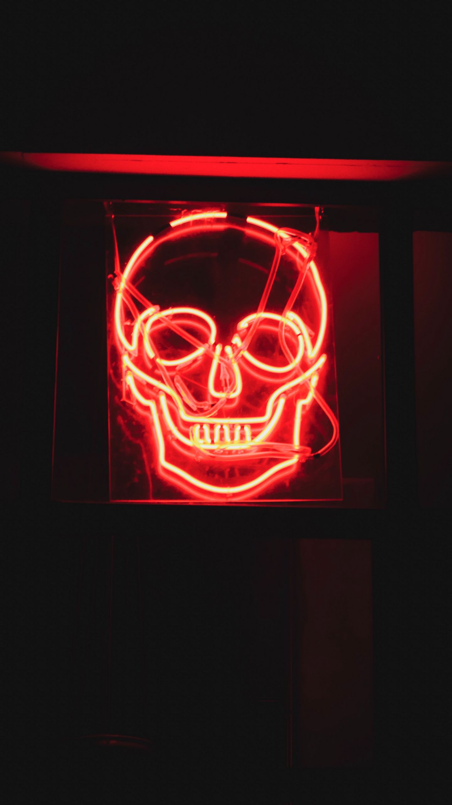 A red neon skull sign on a black background. - Neon orange