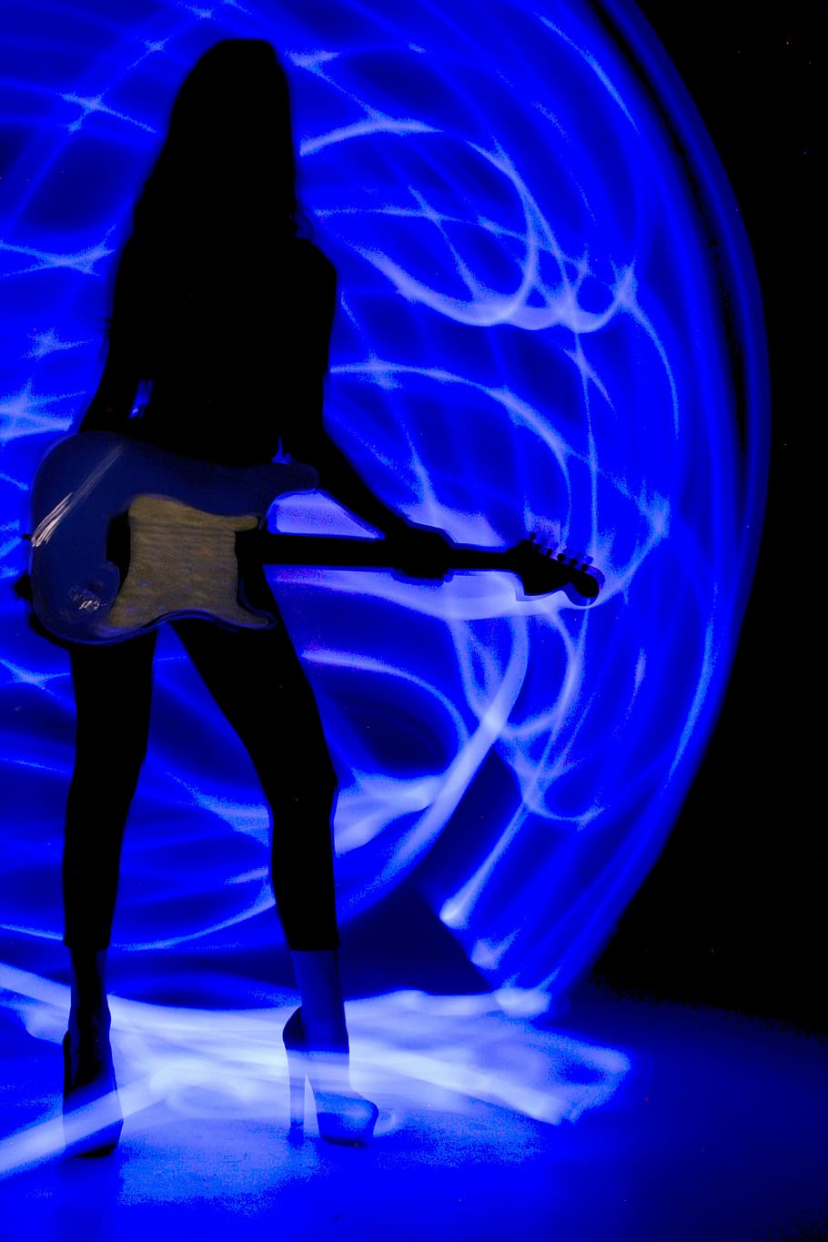 A woman holding a guitar in front of a blue background - Neon blue, guitar