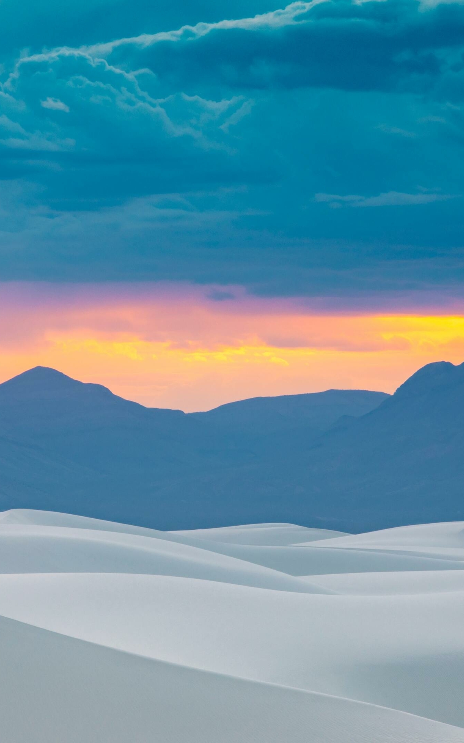 A sunset over white sand dunes with mountains in the background - Desert