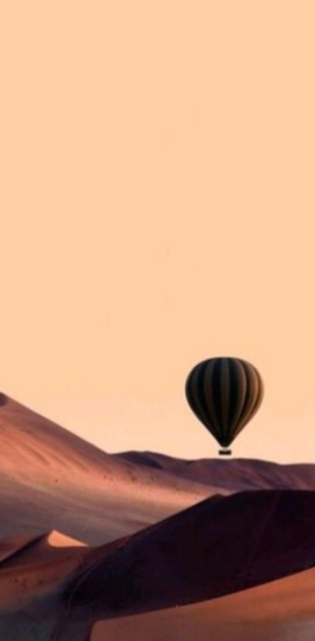 A hot air balloon floating over sand dunes - Desert