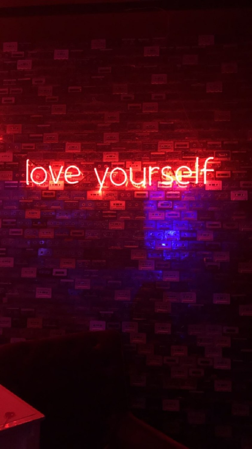 A neon sign that says love yourself on a brick wall - Light red
