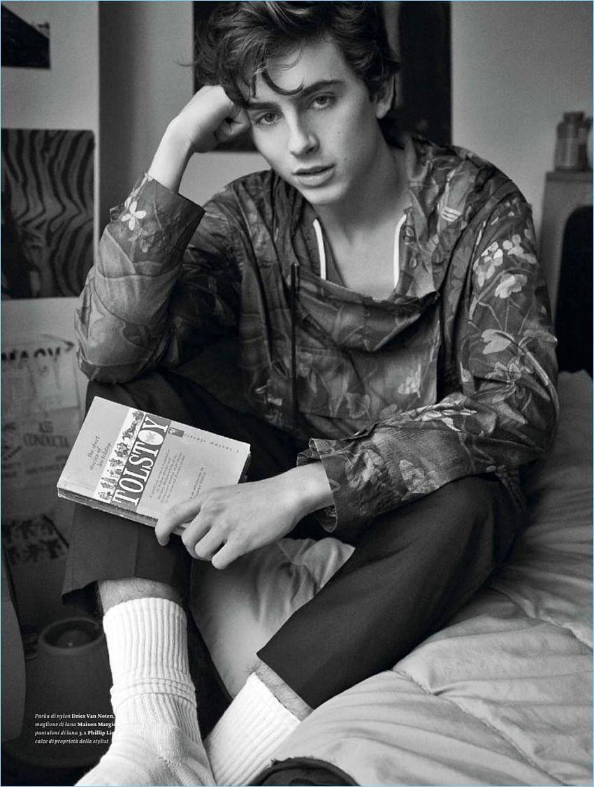 A young man sitting on his bed with an open book - Timothee Chalamet
