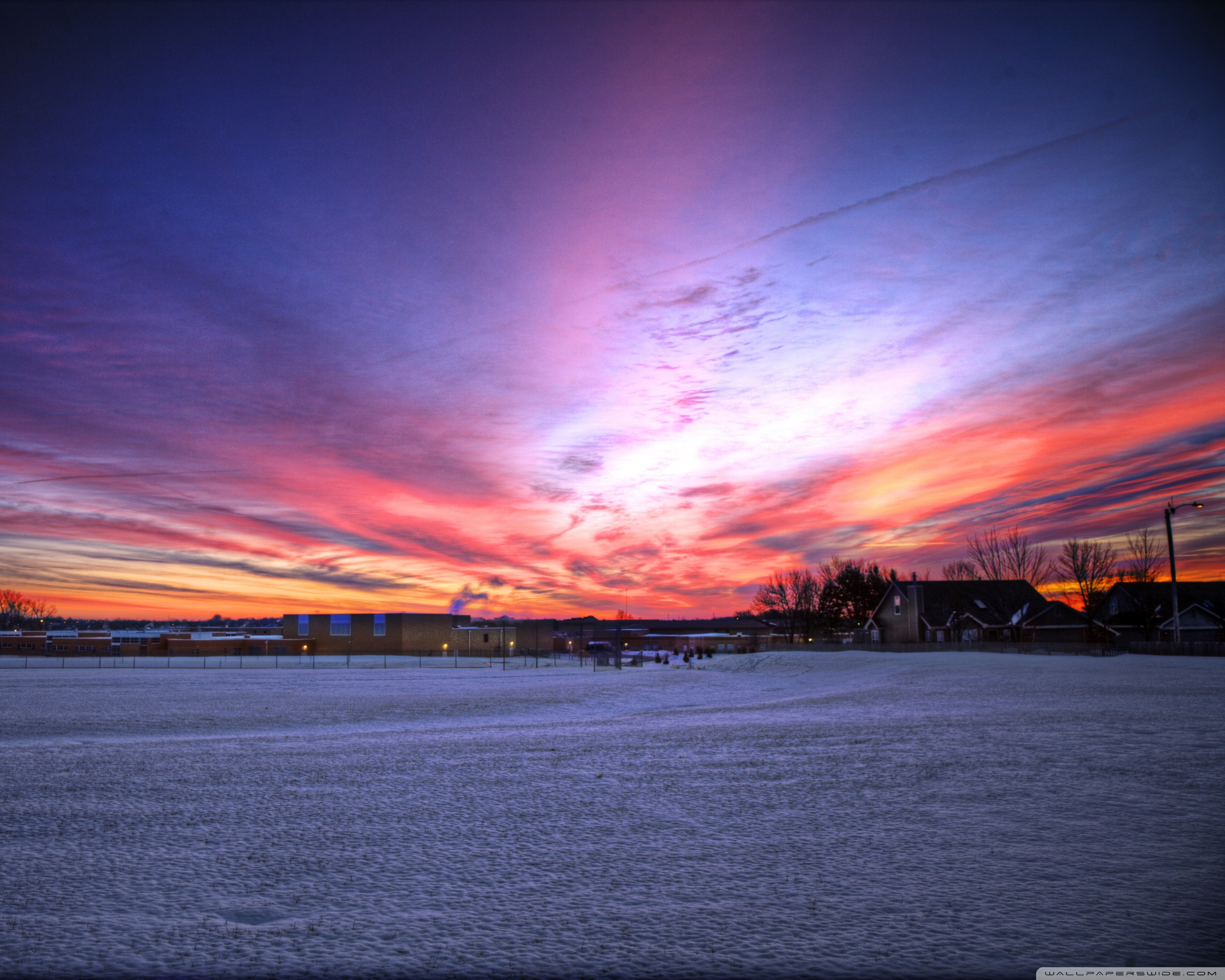 A beautiful sunset over a snowy field with a building in the distance. - Sunrise