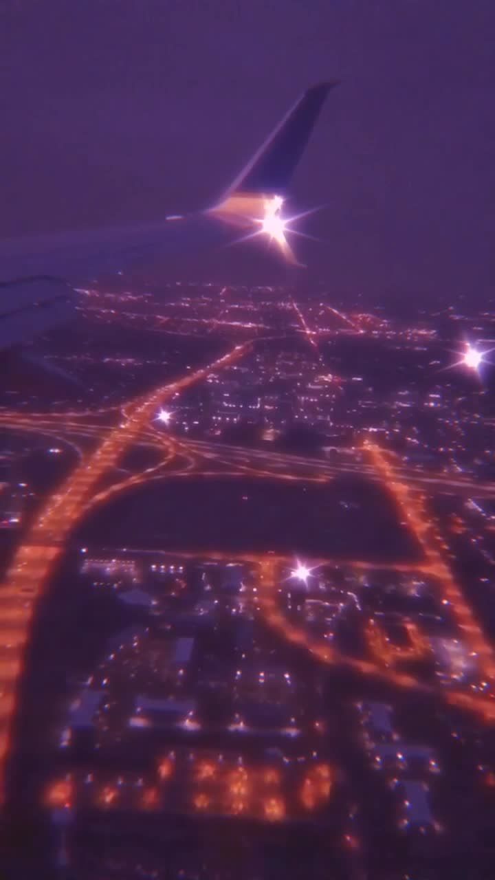 A city lit up at night with a plane's wing in the corner. - TikTok
