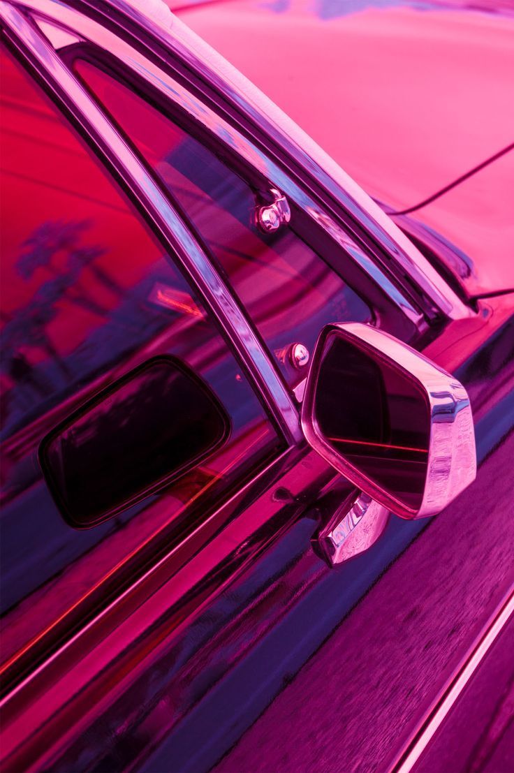 A close-up of a car's side mirror and door handle, shot with a pink light. - Magenta