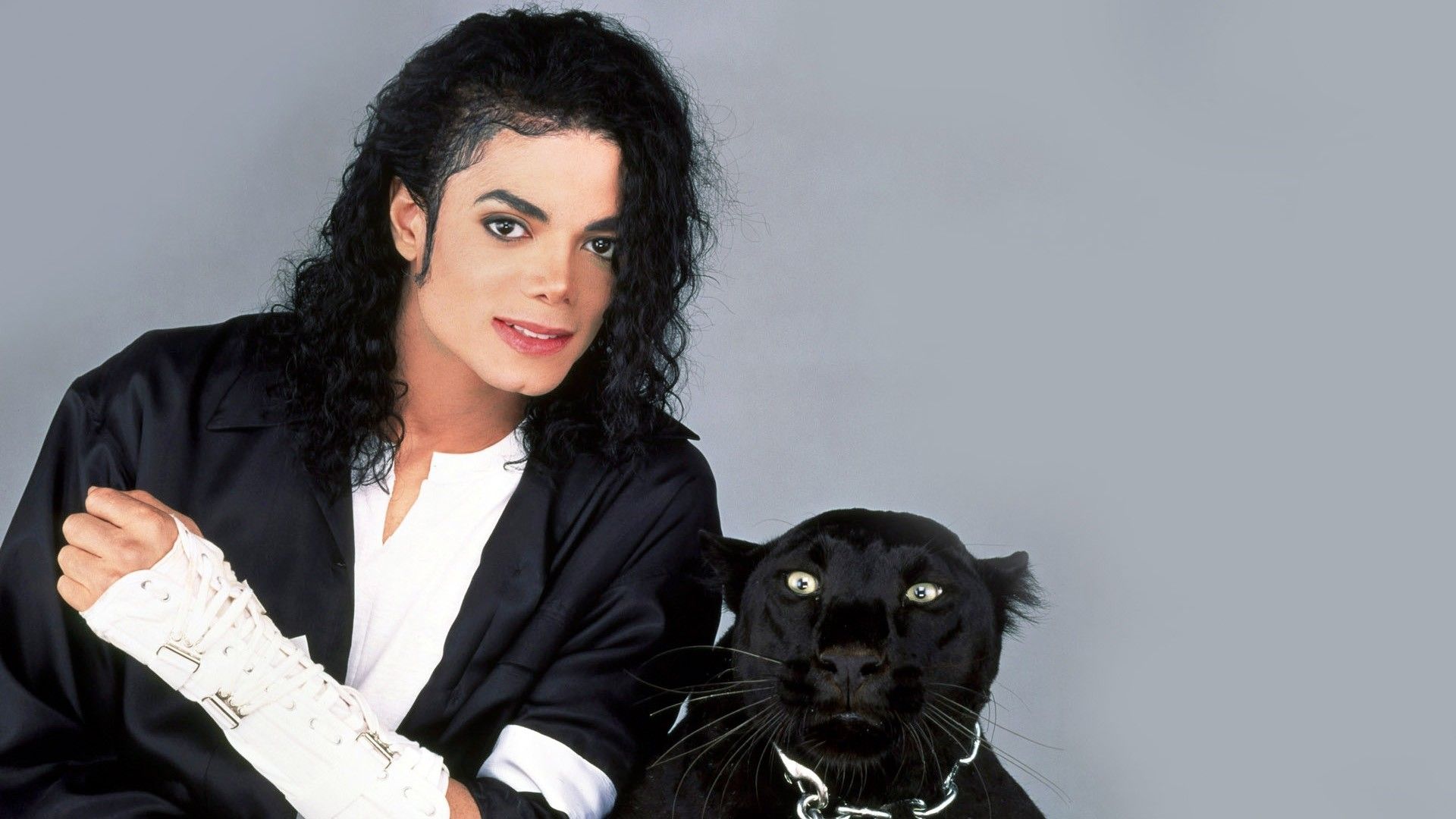 A man in black sitting with his hand on the head of an animal - Michael Jackson