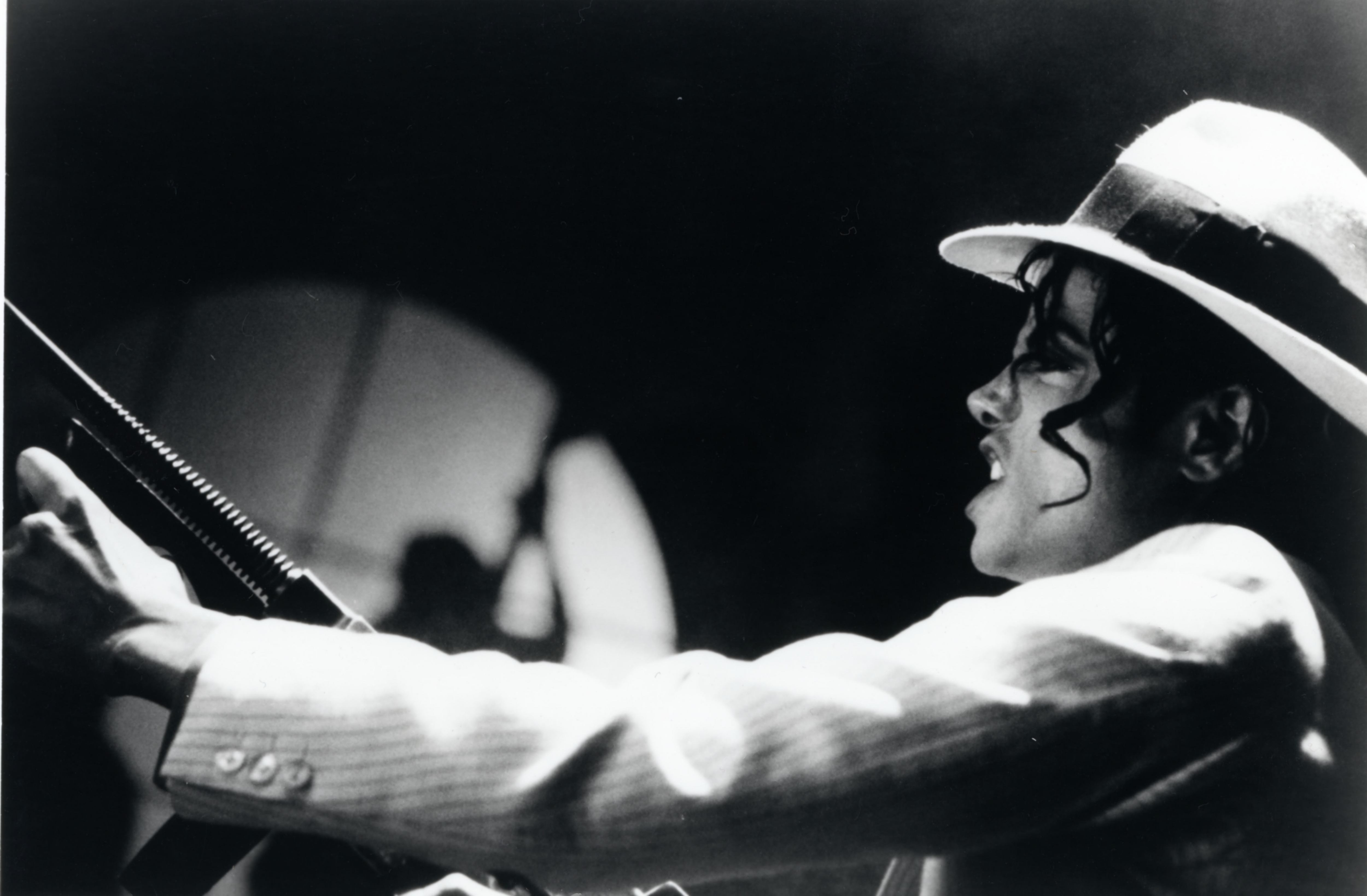 Michael Jackson, wearing a white hat and white jacket, holds a microphone. - Michael Jackson