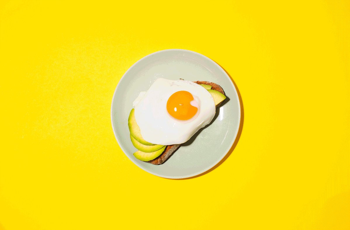 A plate with a fried egg and avocado on toast on a yellow background - Food