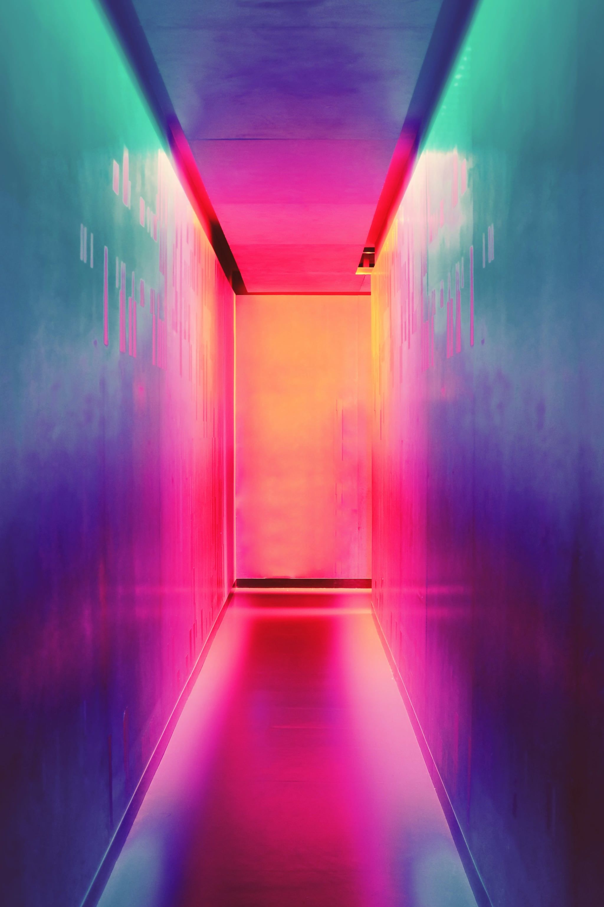 A long, narrow, colorful hallway with pink, purple, and green lighting. - Bright, neon pink