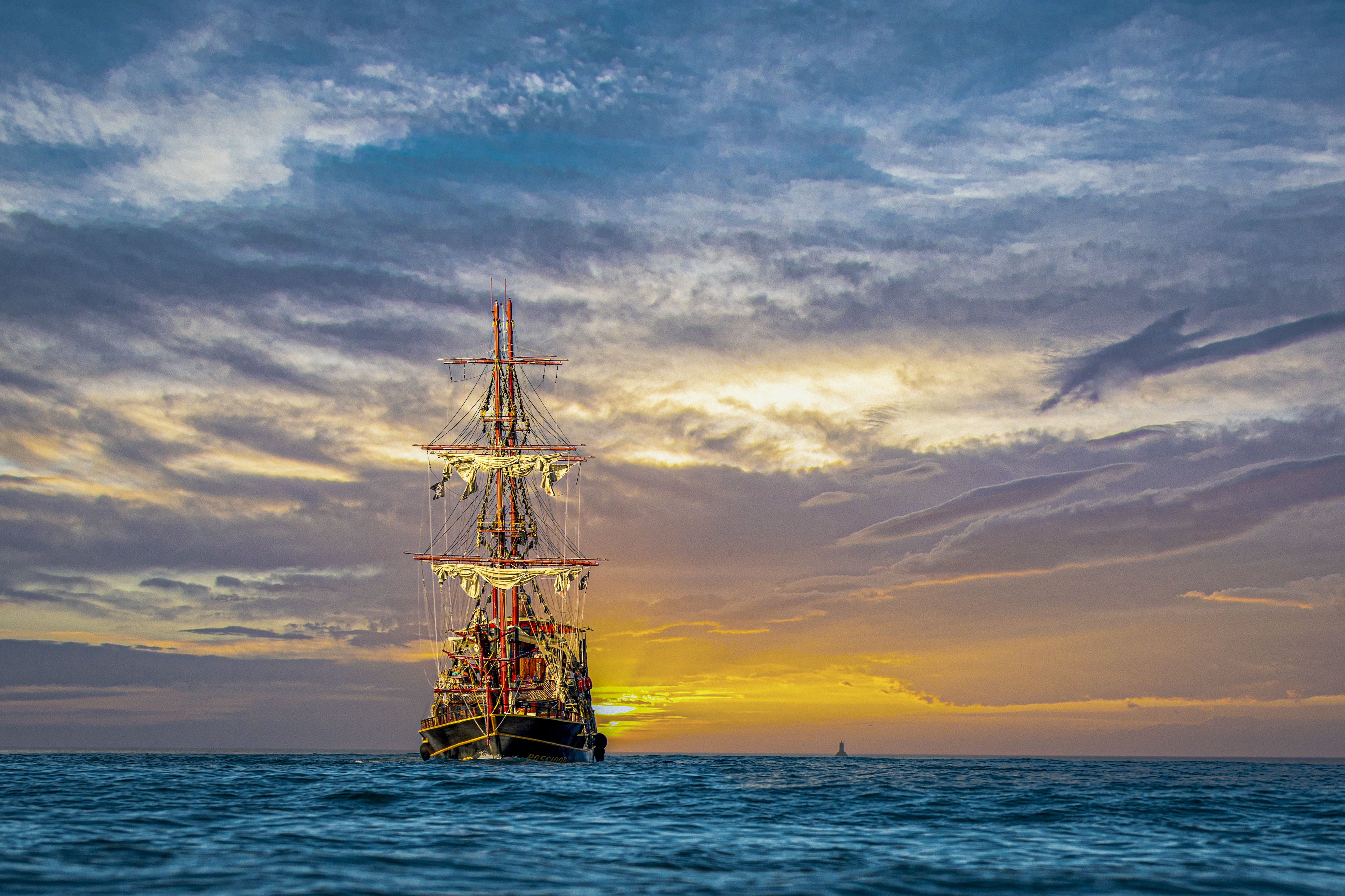 A ship sails on the ocean during a sunset. - Pirate