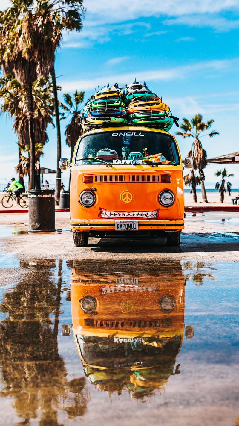 A yellow van with surfboards on top is reflected in a puddle. - Hawaii