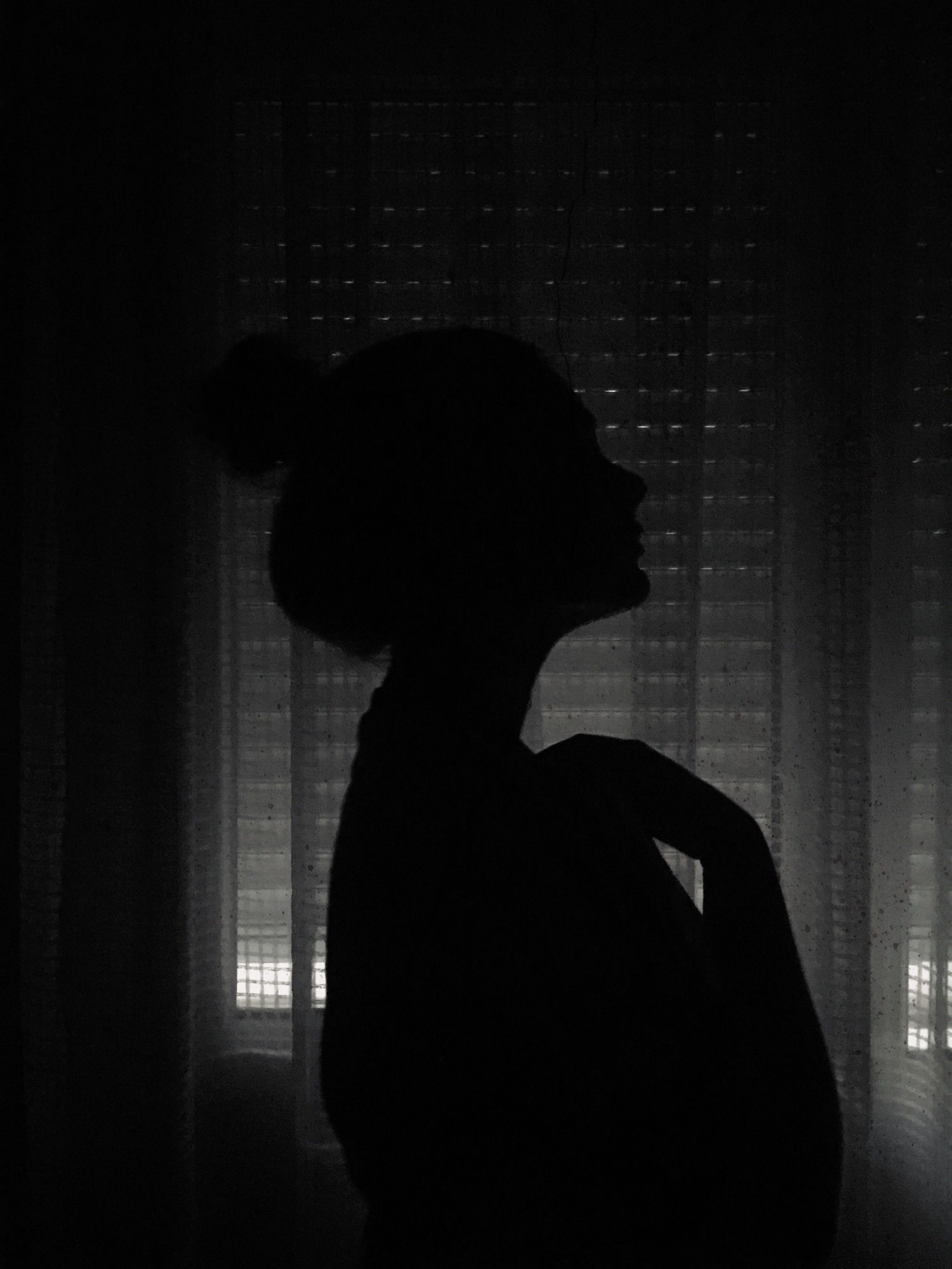 A woman standing in front of window with light - Shadow