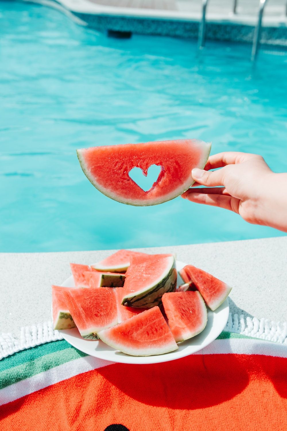 A person holding watermelon slices in front of the pool - Watermelon