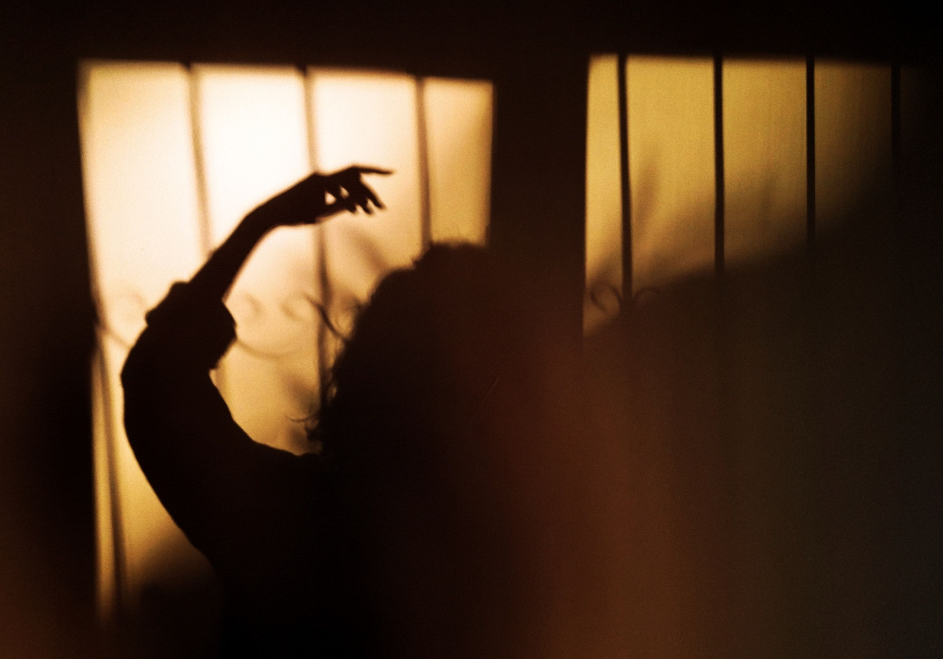 A woman's silhouette against a window, with her arm outstretched. - Shadow