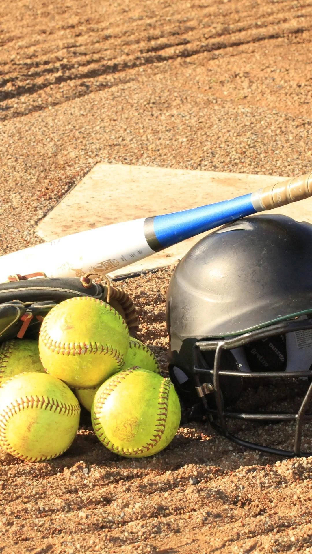 A softball bat, helmet, and glove sitting on the ground - Softball