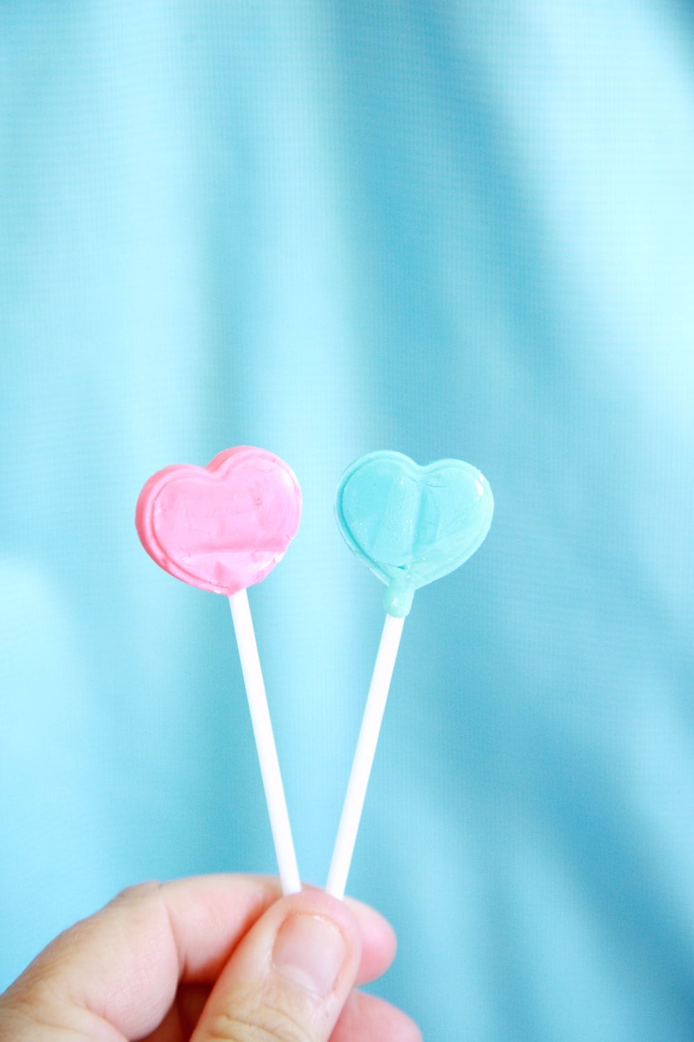 A person holding two lollipops in the shape of hearts - Candy