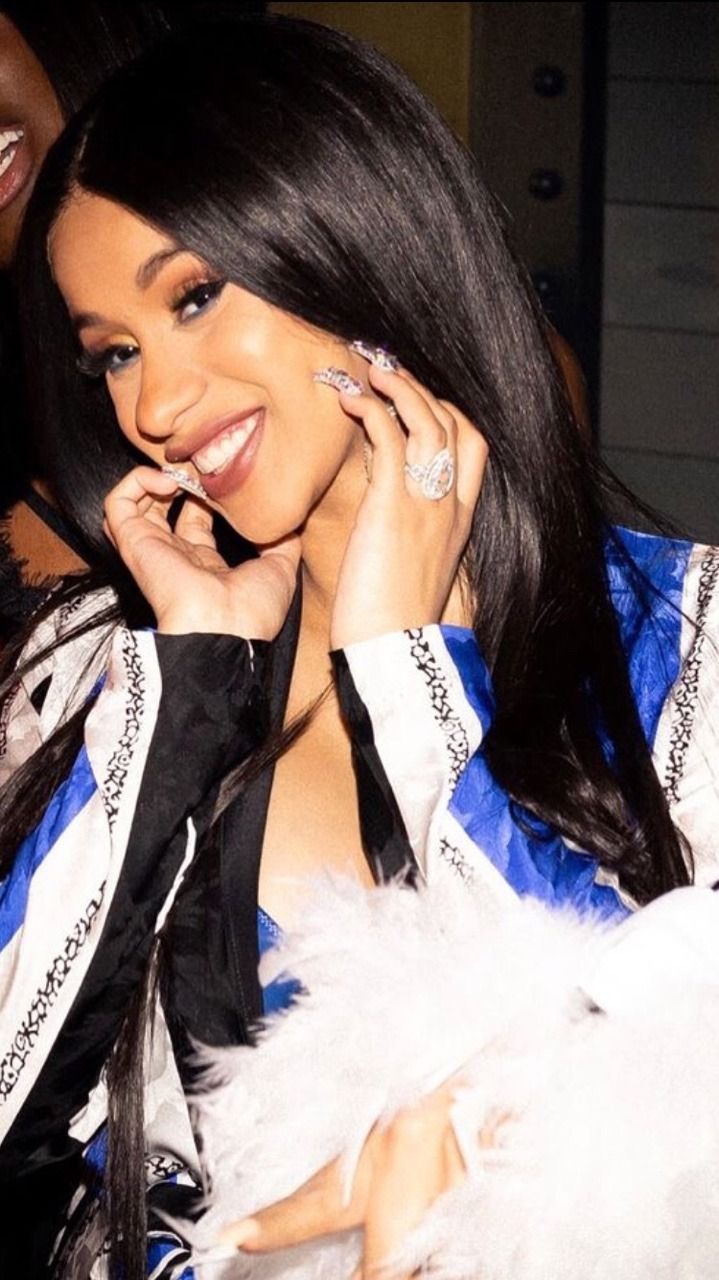 Cardi B with long black hair, wearing a blue and white top and a black and white jacket. - Cardi B