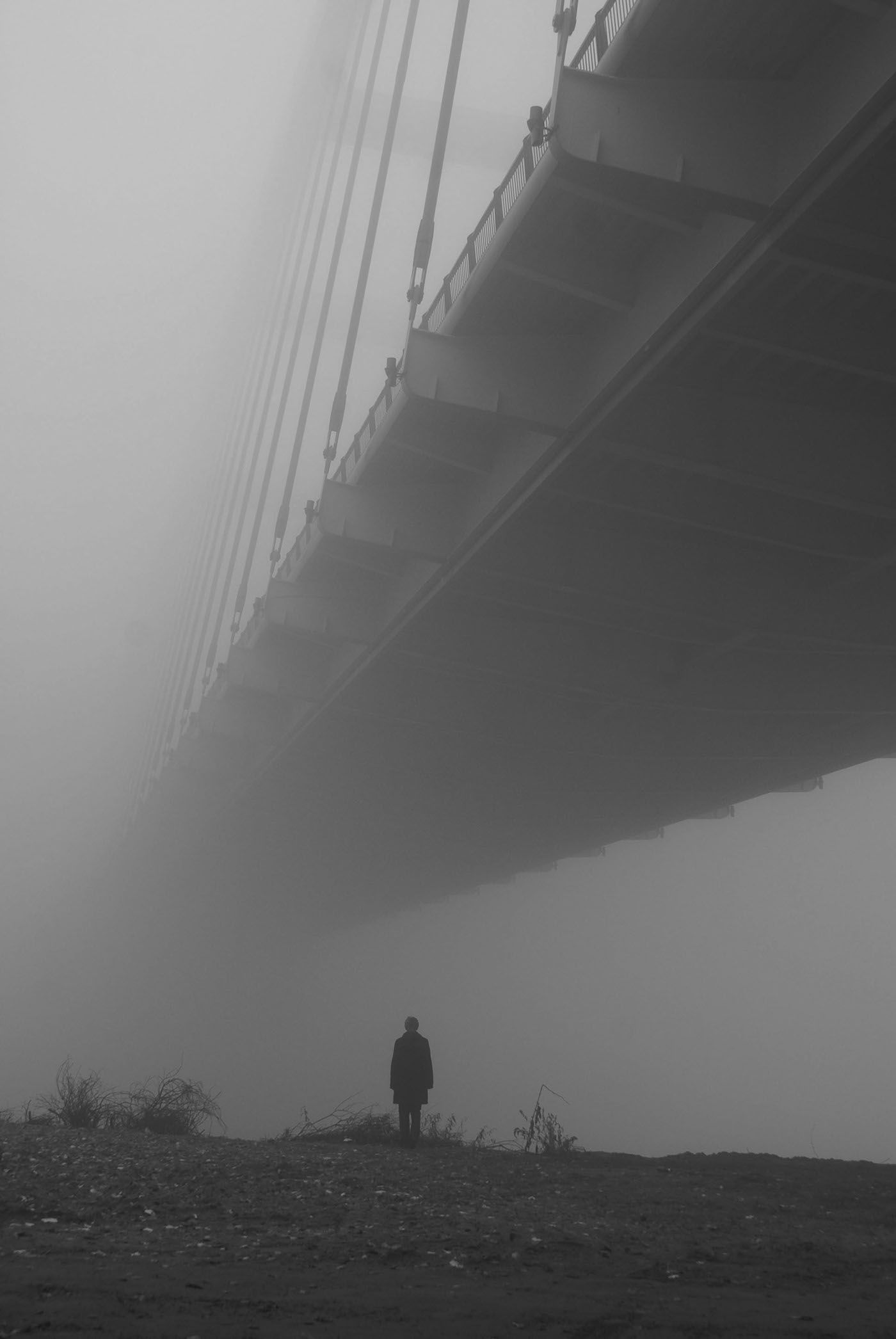 A man in a suit stands under a bridge in the fog. - Fog