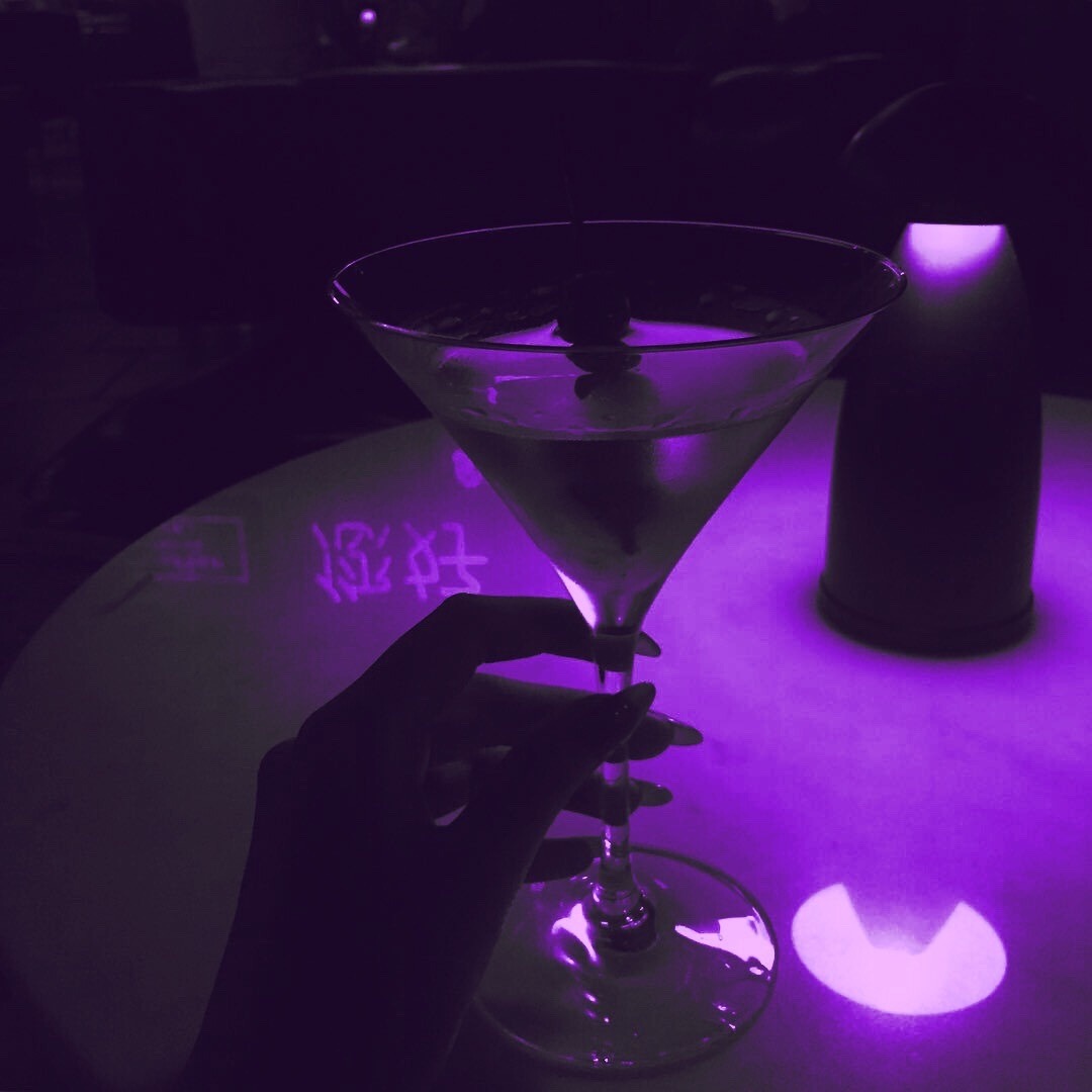 A purple lit bar with a hand holding a martini glass - Neon purple