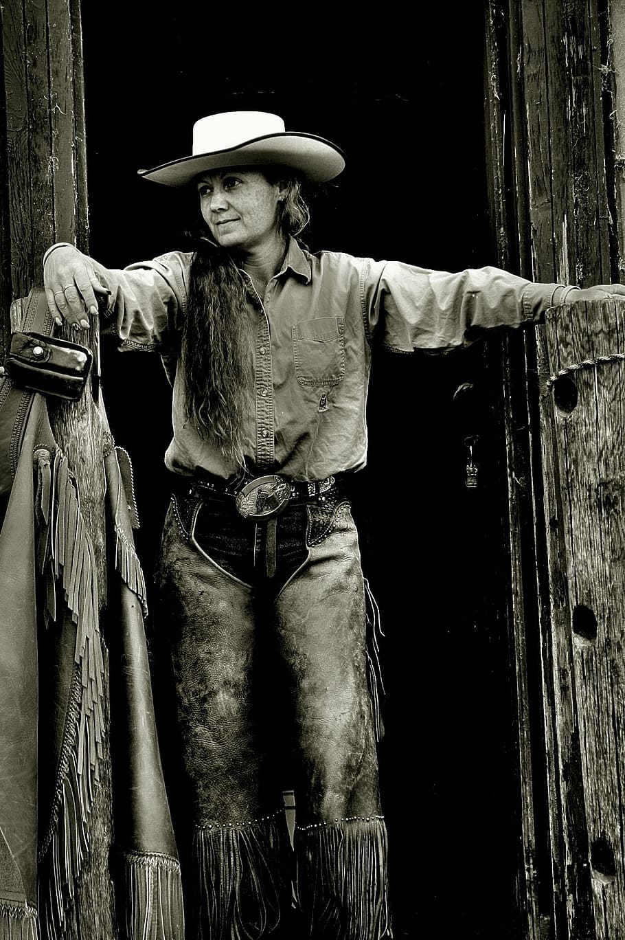 A woman in chaps and a cowboy hat stands in a doorway. - Cowgirl