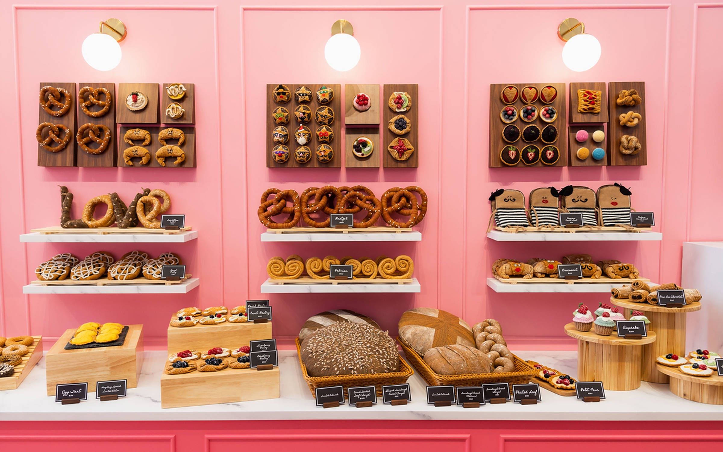 A pink wall with shelves of different types of pastries. - Bakery