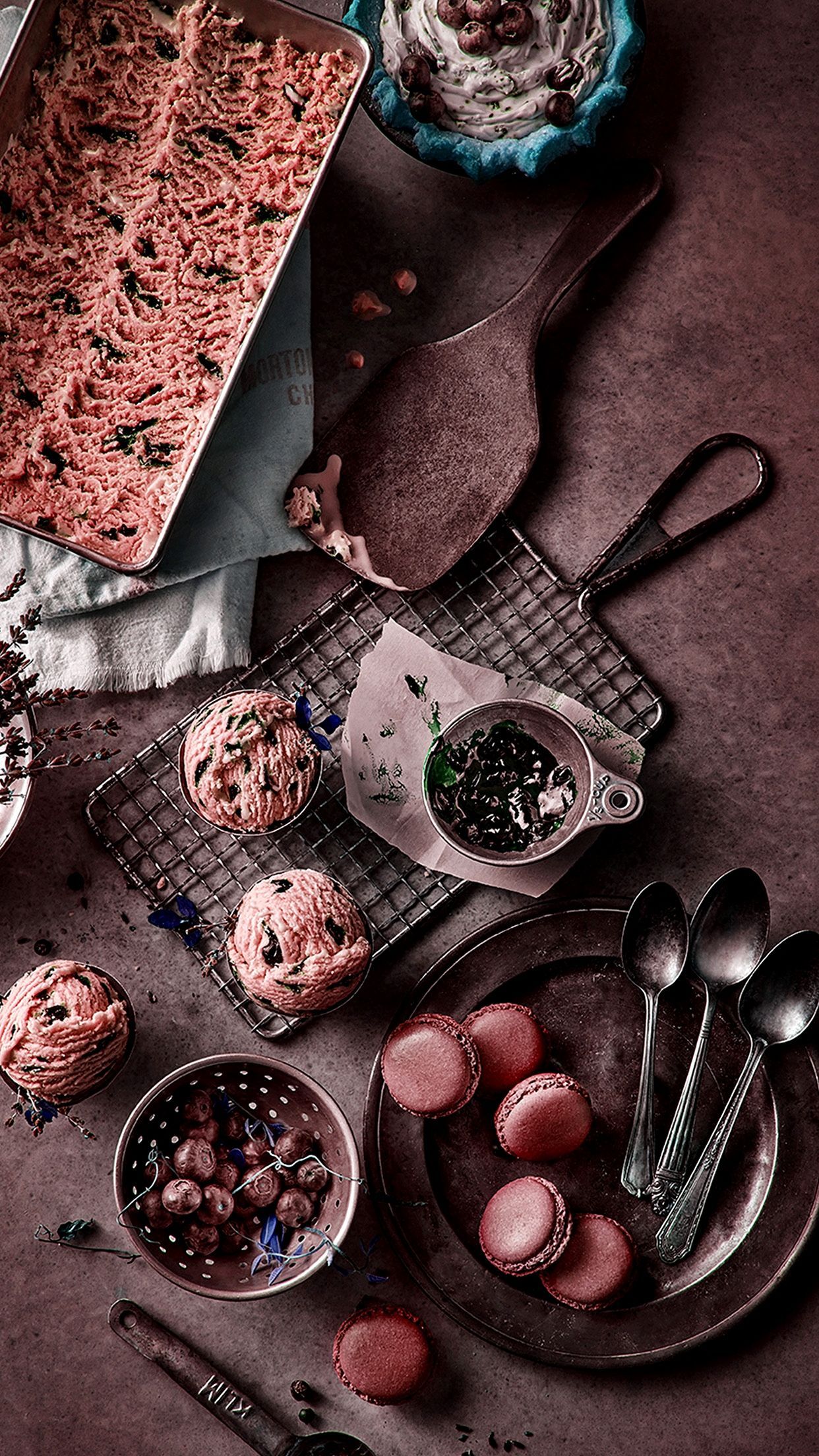 Pink ice cream in a metal pan with spoons and bowls of toppings. - Bakery