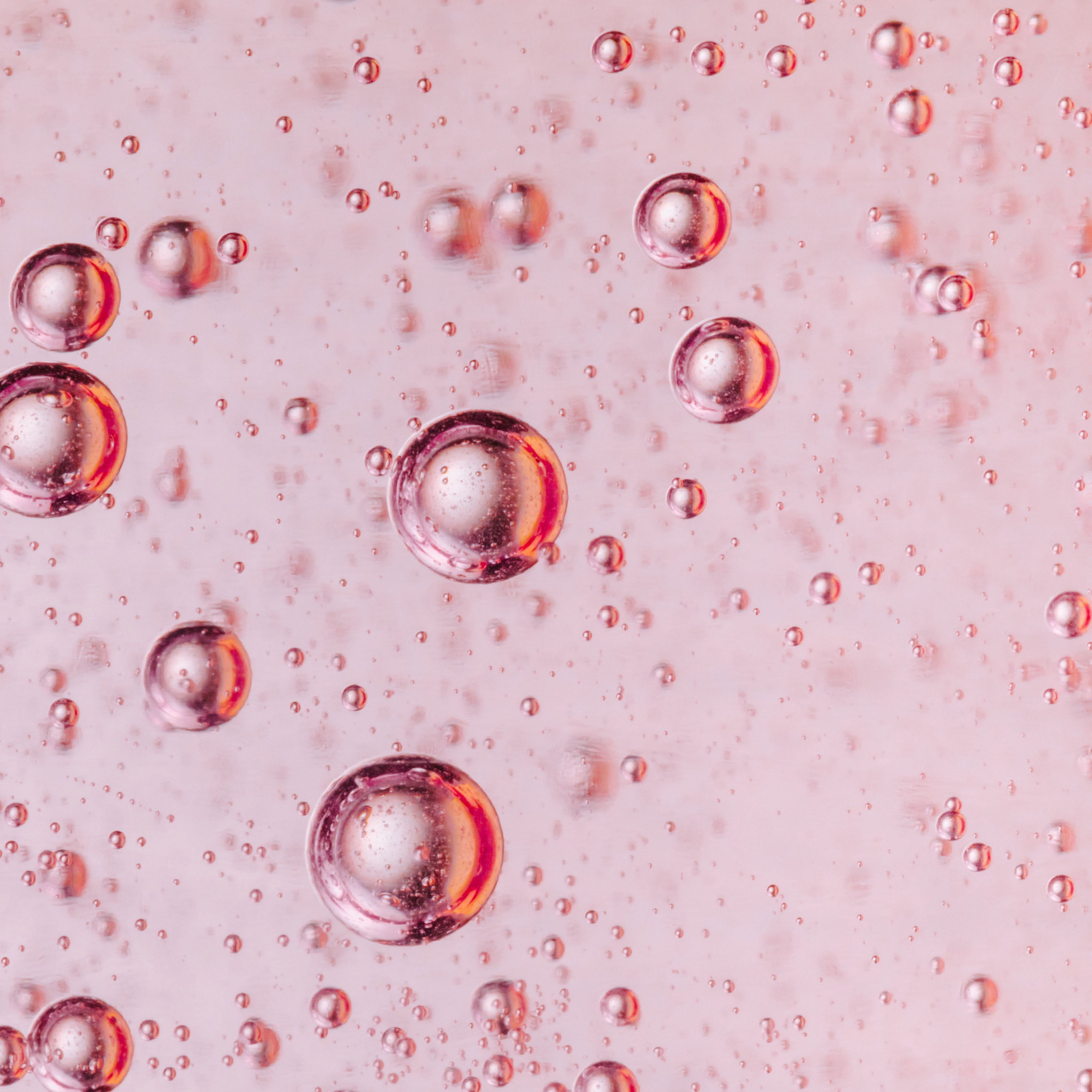 A close up of droplets of liquid on a pink background - Bubbles