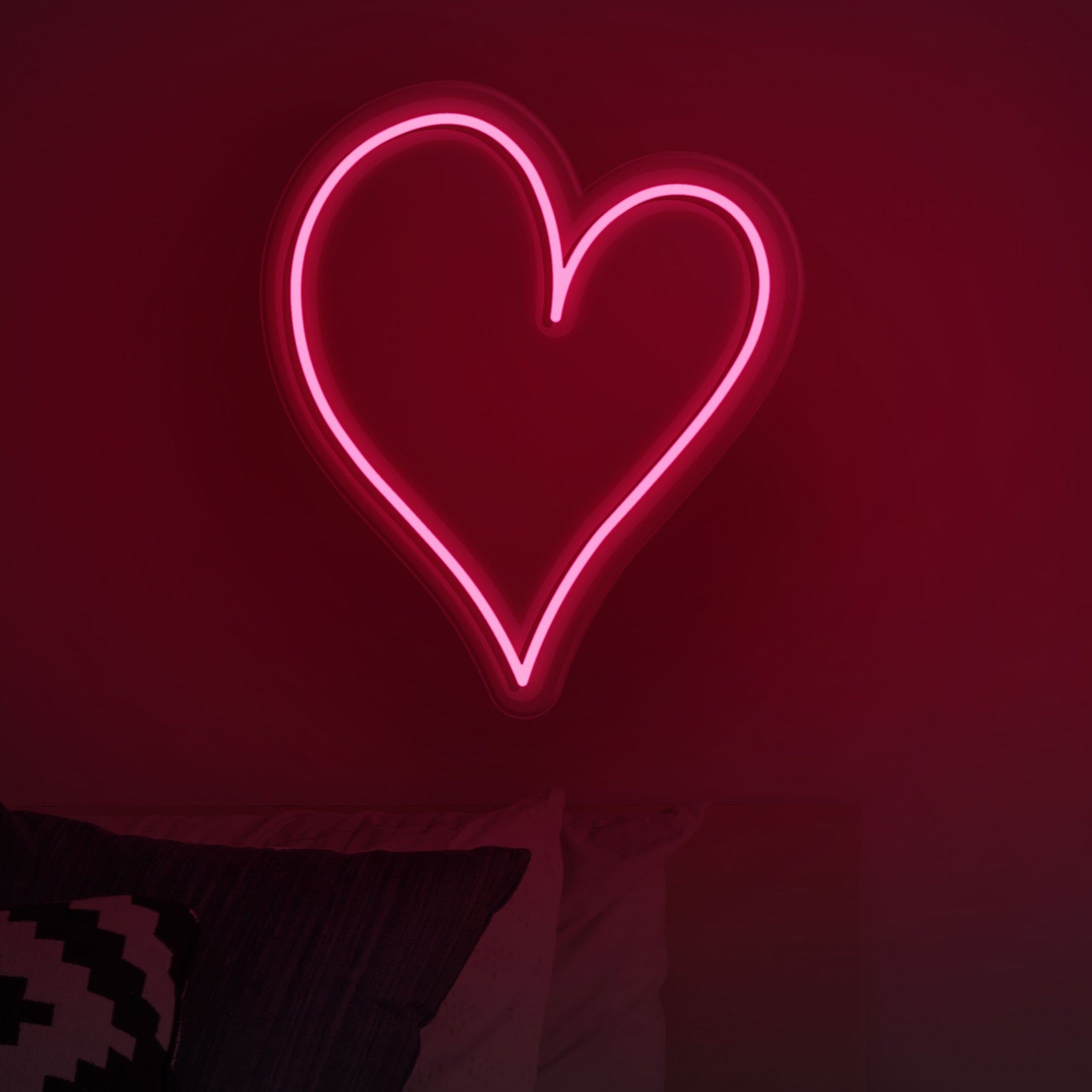 A neon heart shaped light is on the wall - Neon red