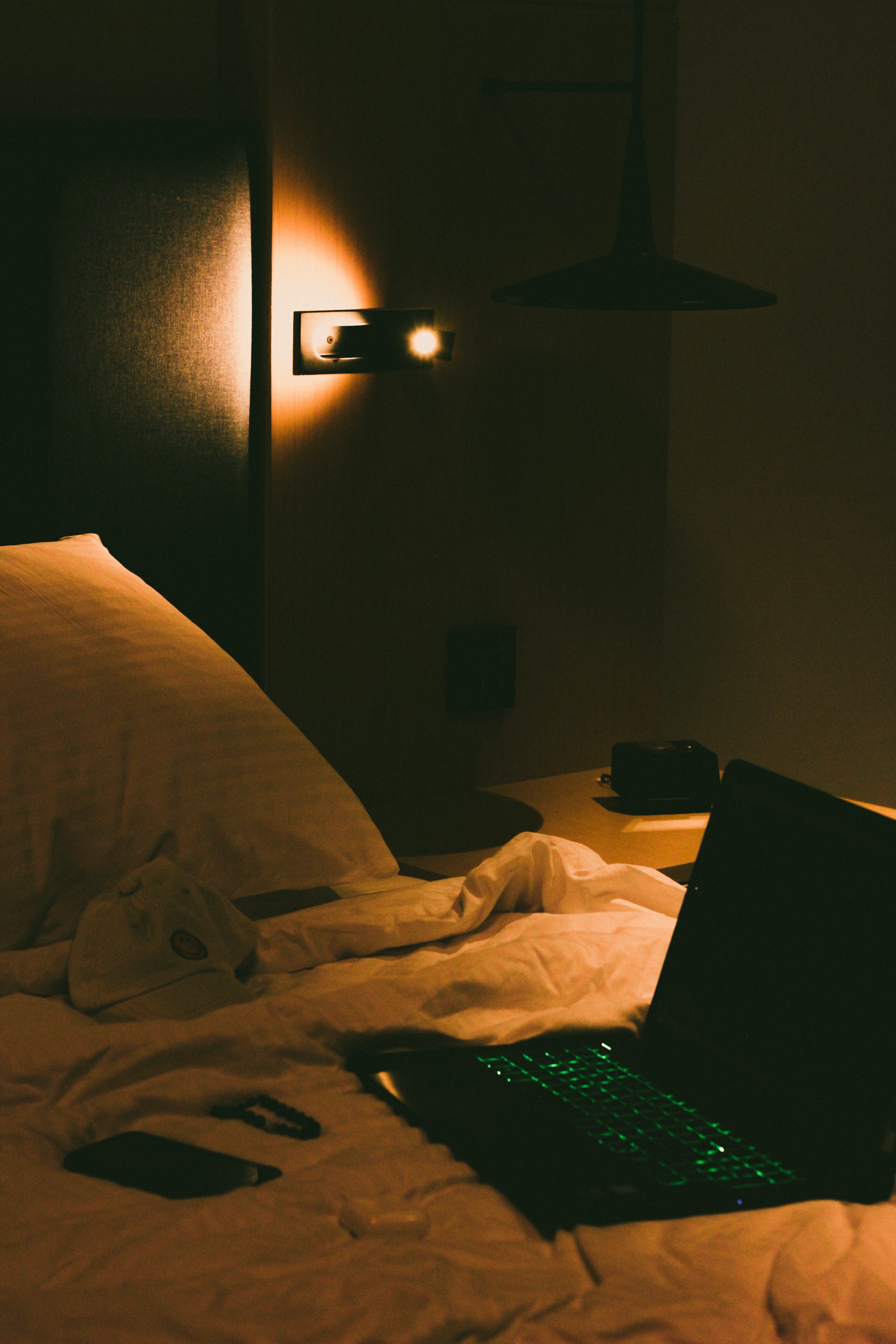 A bed with a laptop, a cup, and a cell phone on it. - Dark