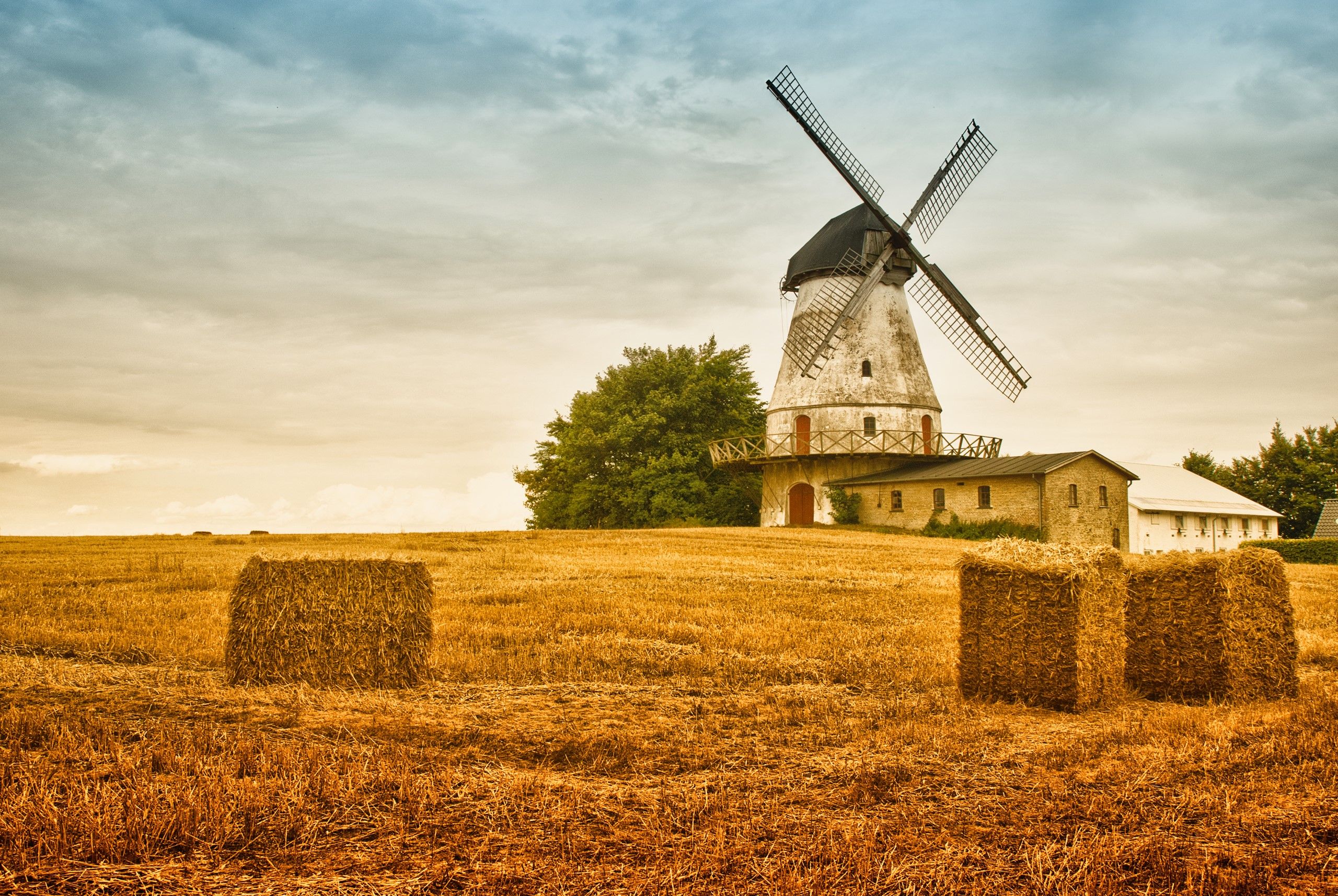 A windmill and hay bales in the middle of an open field - Farm
