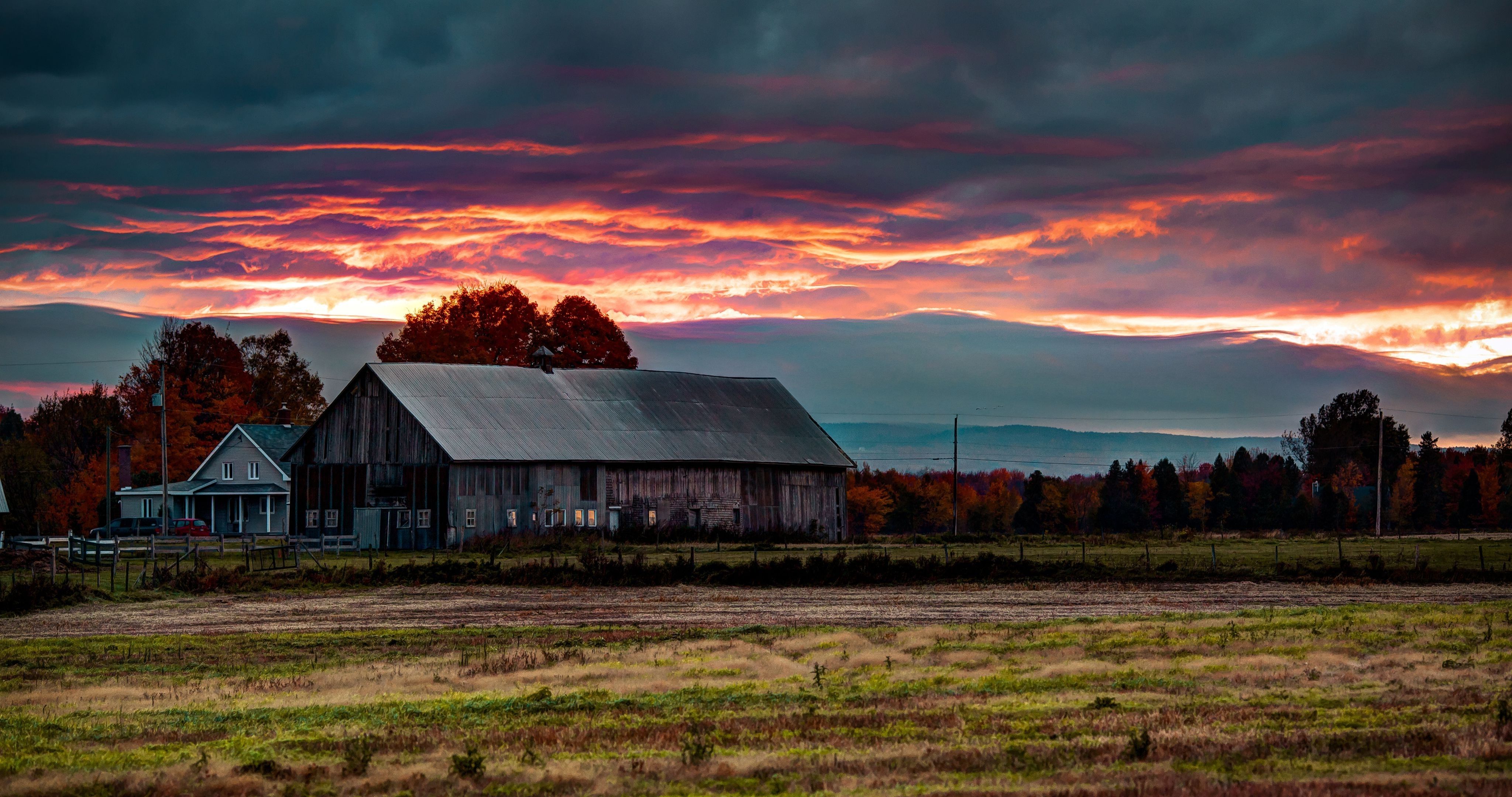 A barn sits in a field with a beautiful sunset in the background. - Farm