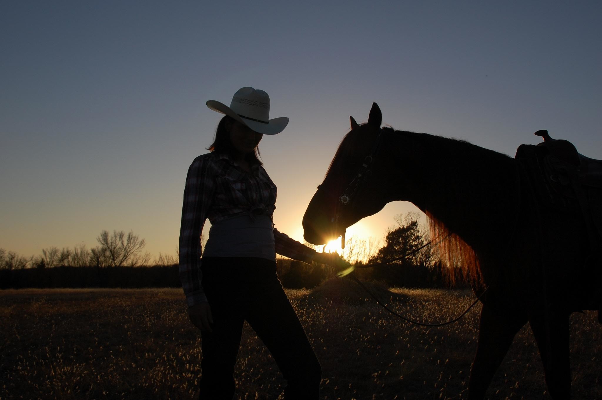 A woman in cowboy hat standing next to horse - Cowgirl