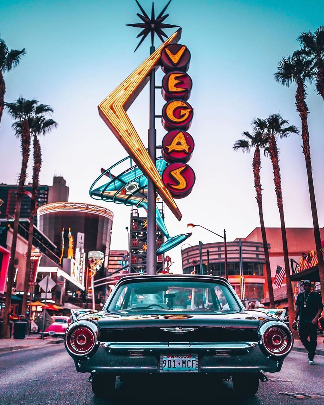 A classic car driving down the street in front of the neon sign for the Las Vegas strip. - Las Vegas