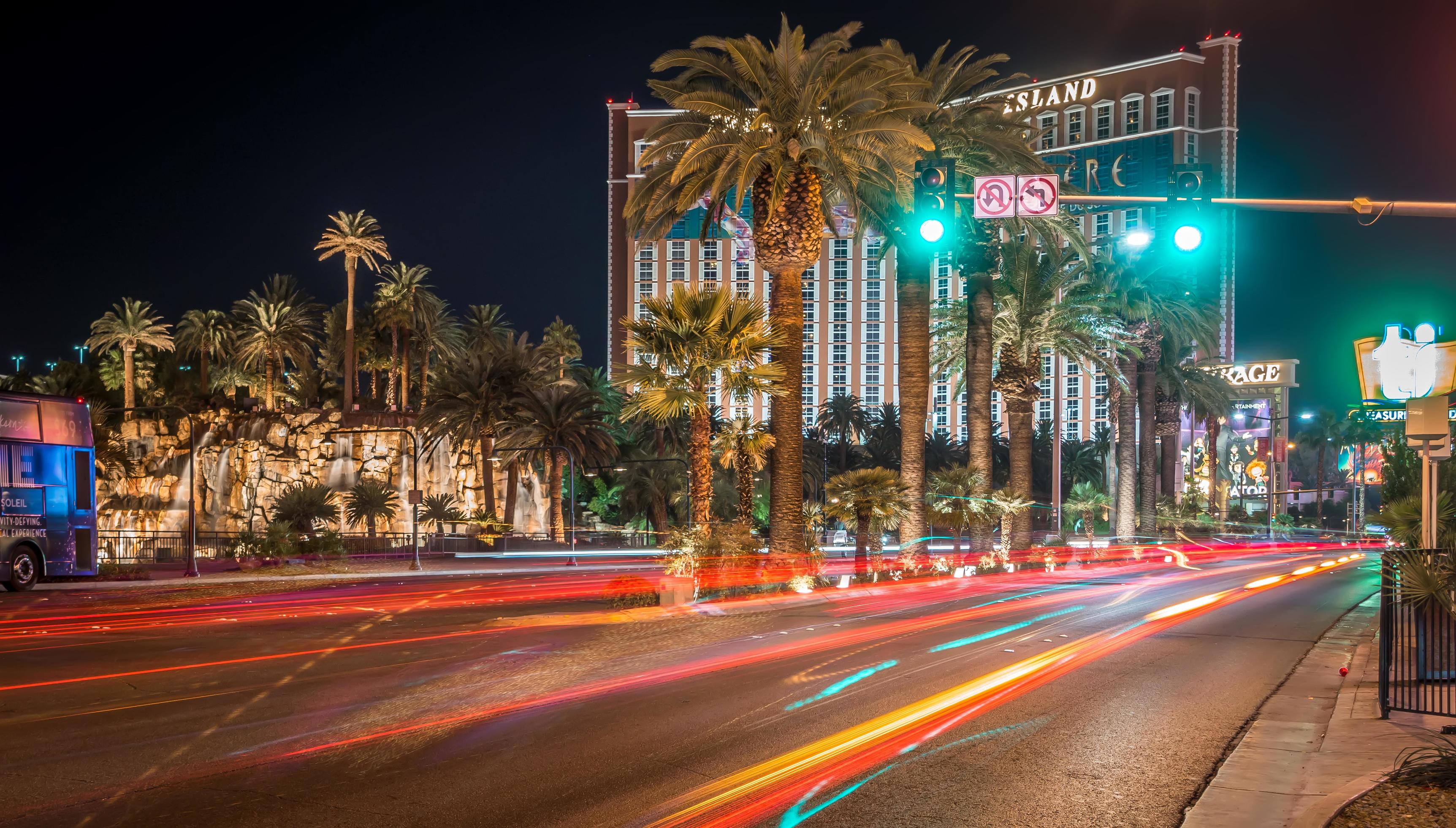A busy street in Las Vegas at night with traffic lights and palm trees. - Las Vegas