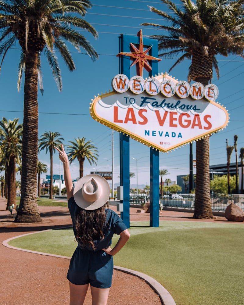 A woman in shorts and hat is standing next to the welcome sign - Las Vegas
