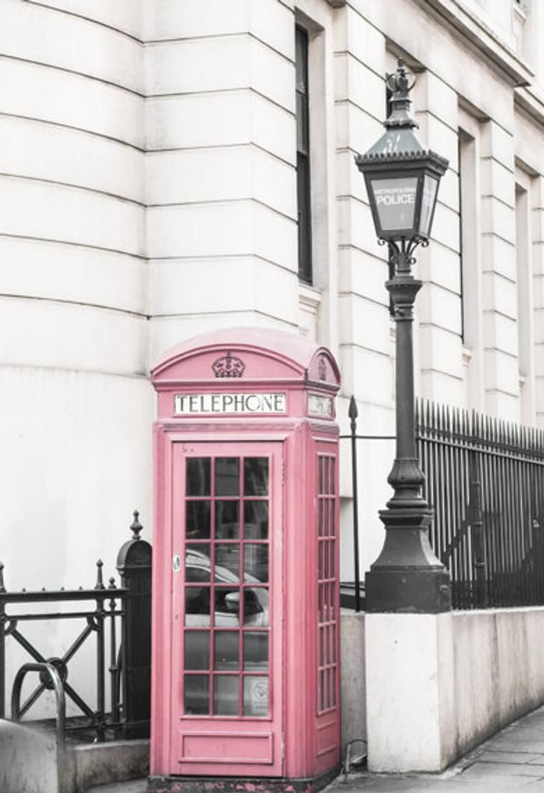 A pink phone booth is in front of an old building - London