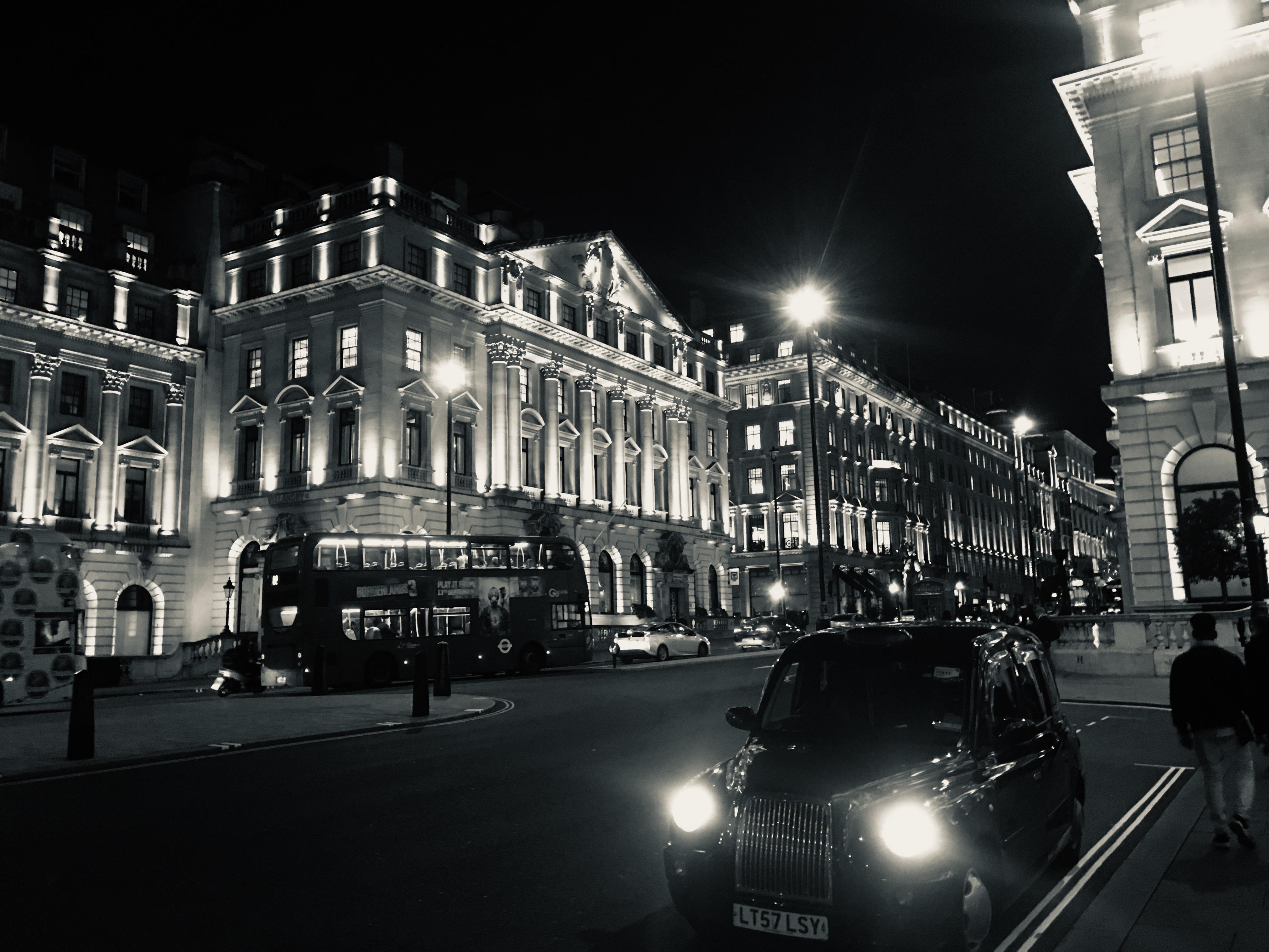 A black cab and a bus drive through the streets of London at night. - London